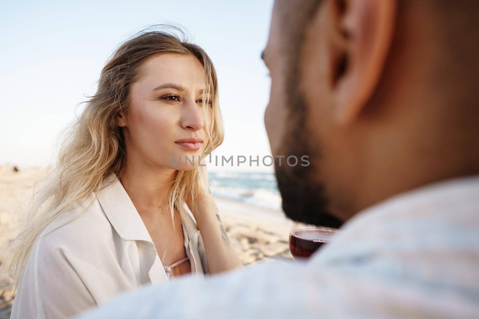 Portrait of a young couple sitting on the beach and drinking wine, close up
