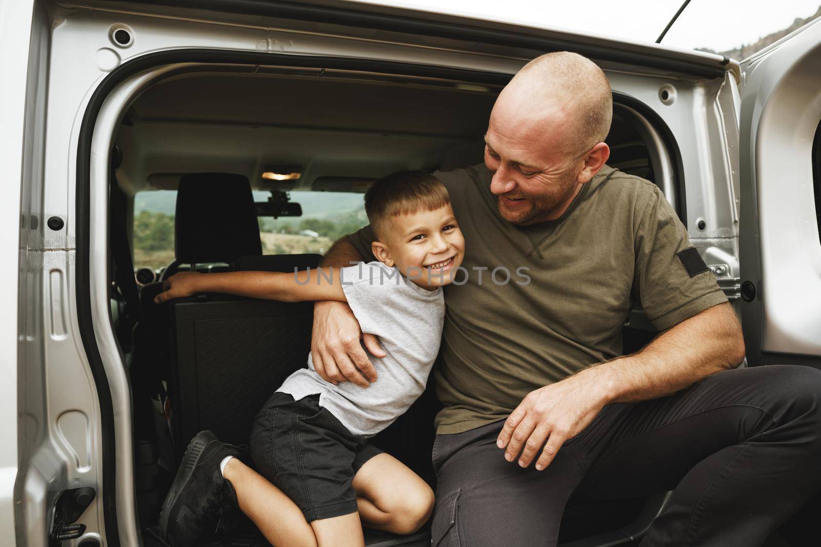 Happy father and son sitting in car trunk on road trip