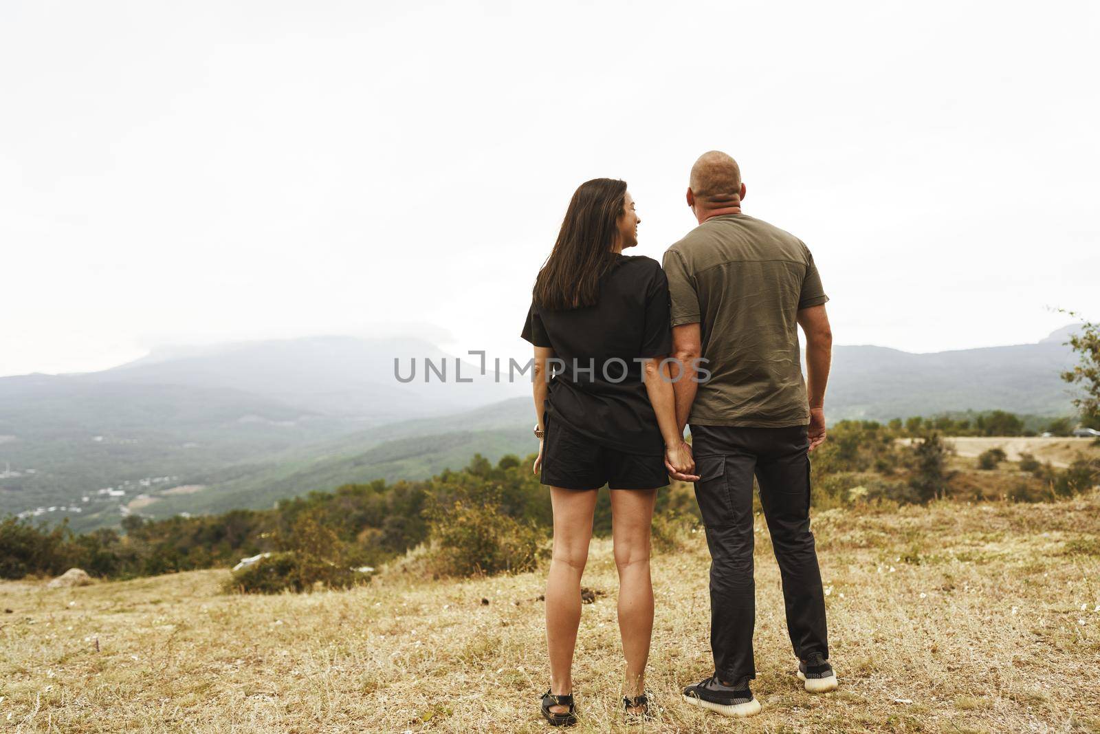 Back view of couple standing and looking at foggy mountains in autumn