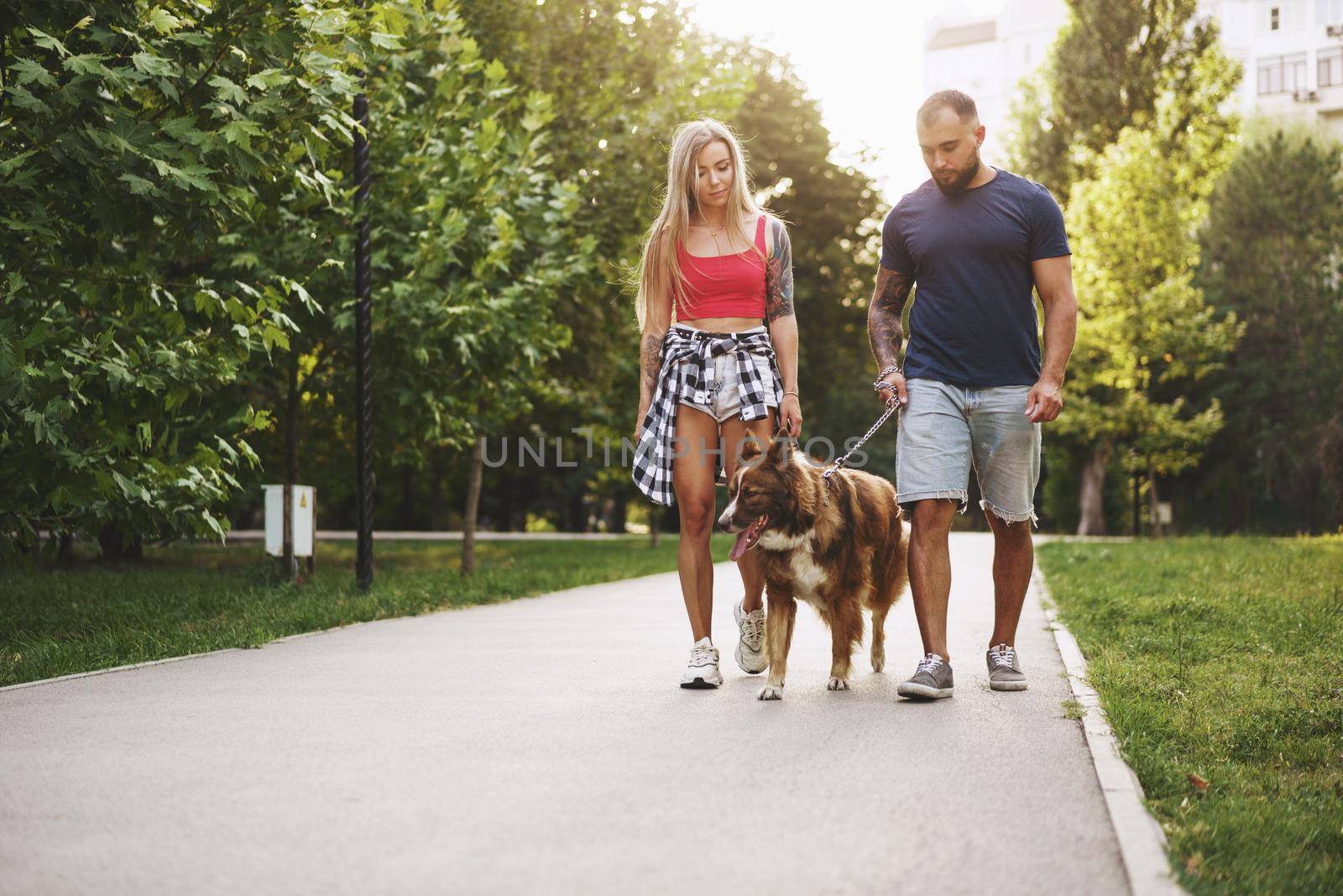 Young beautiful couple walking the dog in the summer park by Fabrikasimf