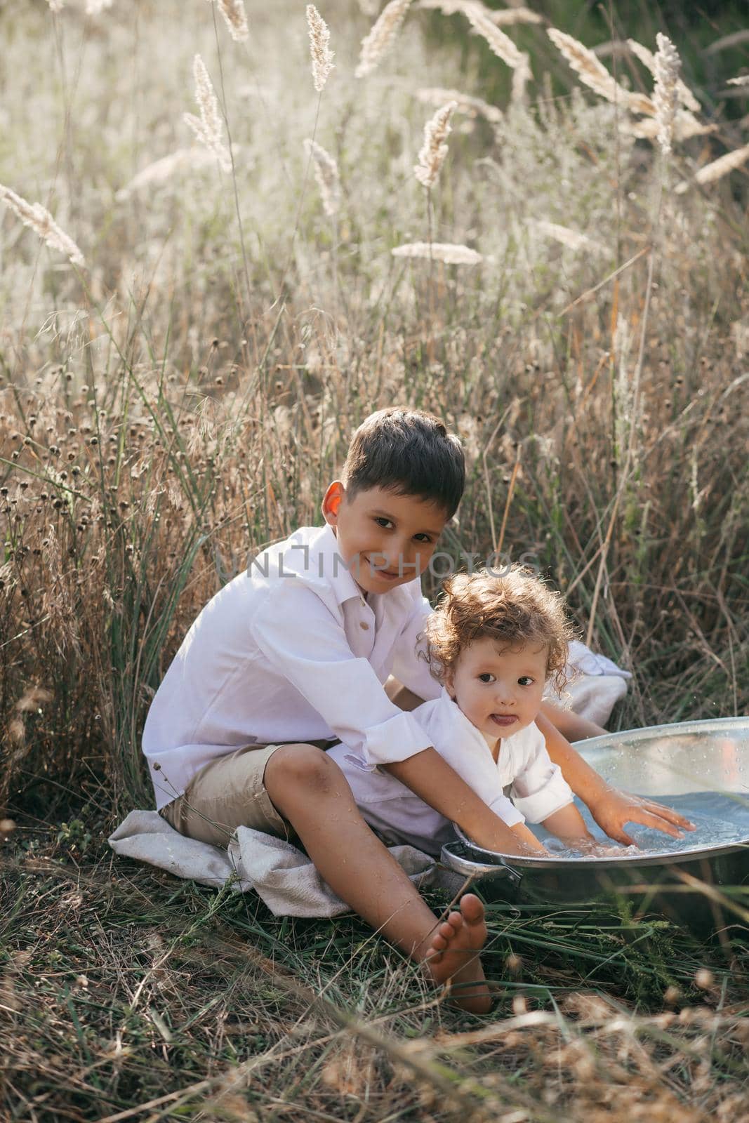 Happy two brothers are playing with water in a basin on wheat summer field. by Forewer