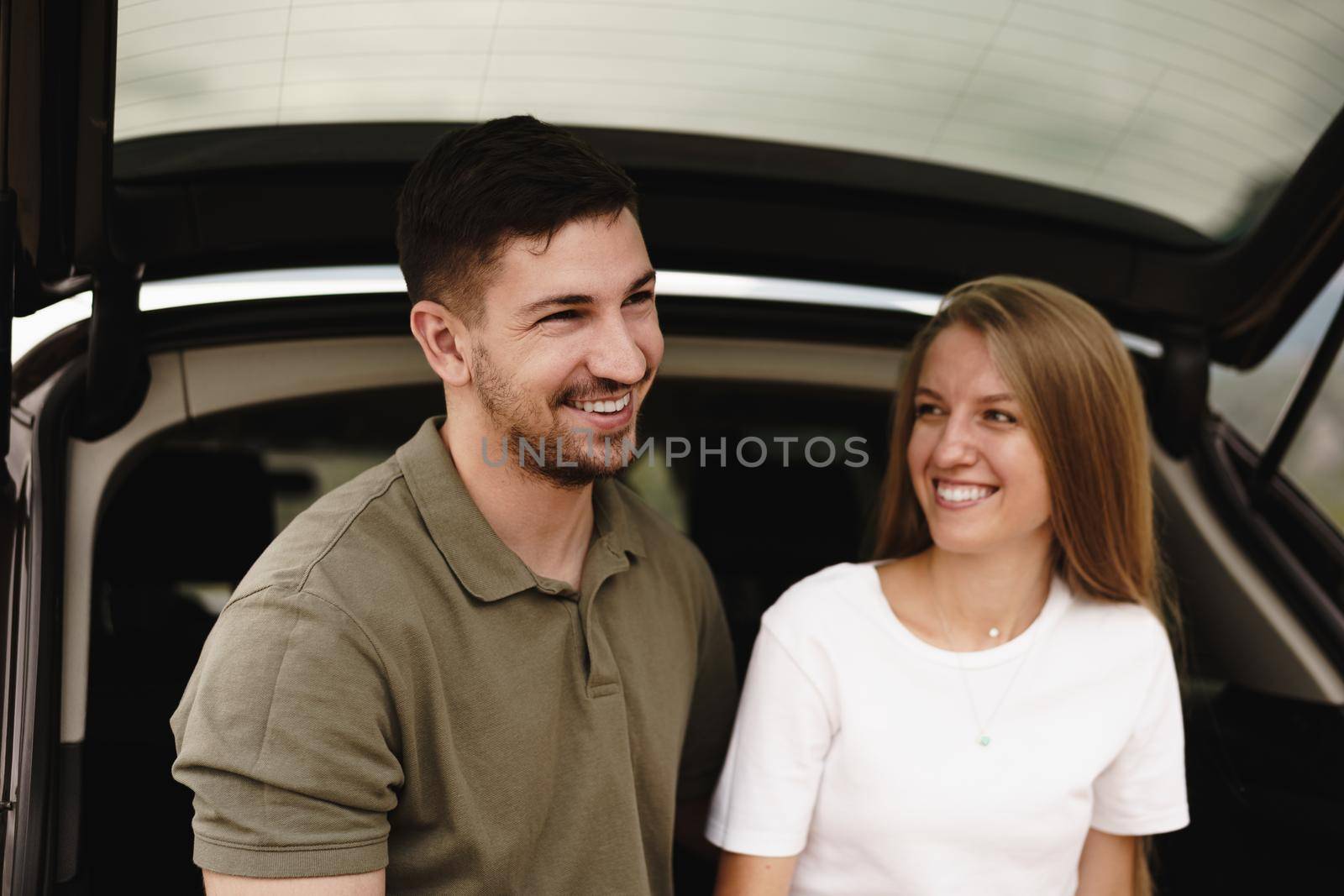 Young happy couple on a road trip sitting in car trunk outdoor