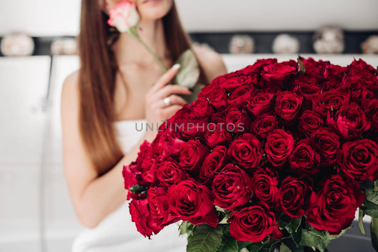 Close-up of bunch of stunning red roses and unrecognizable woman with flower in blurred background.