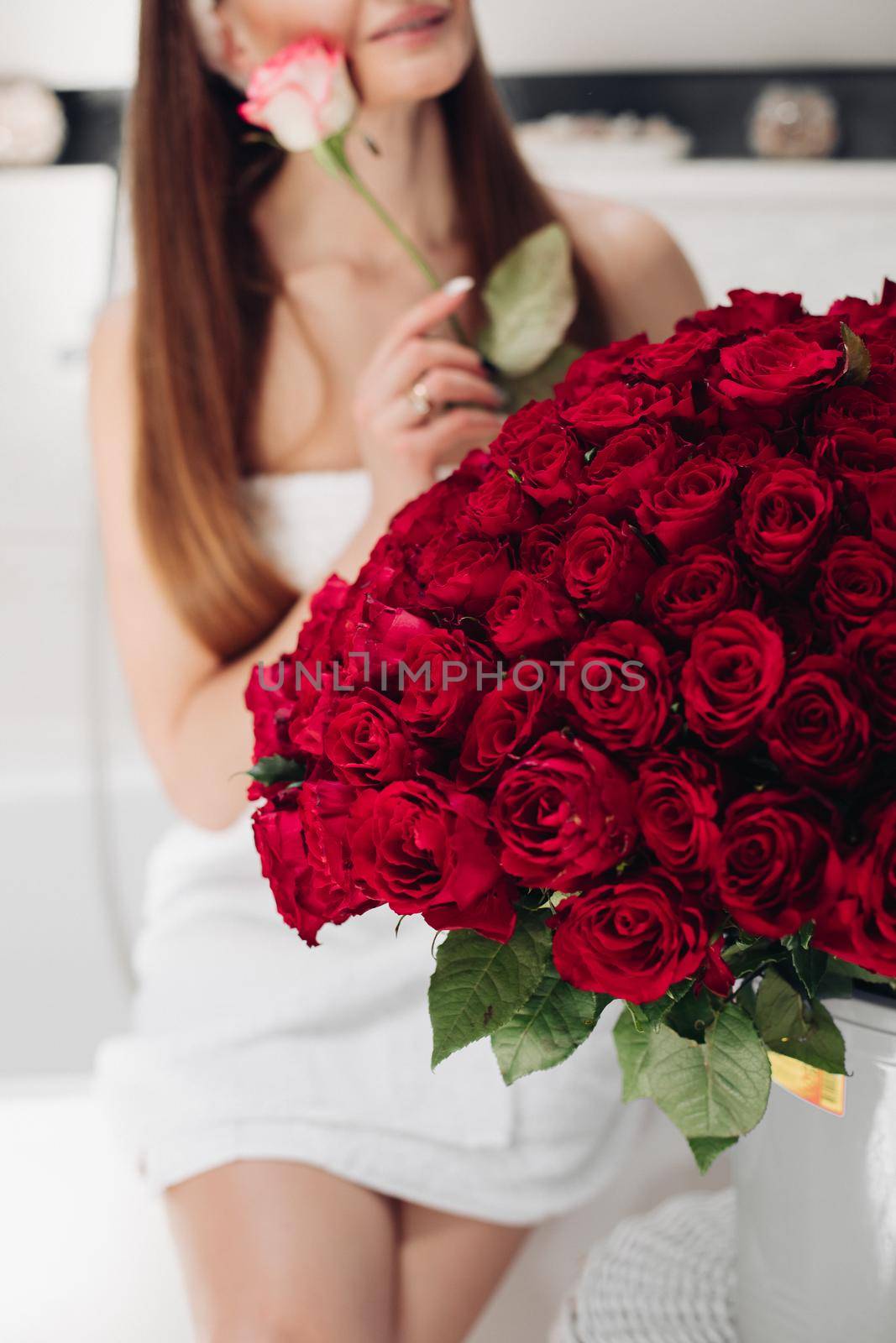 Close-up of bunch of stunning red roses and unrecognizable woman with flower in blurred background.