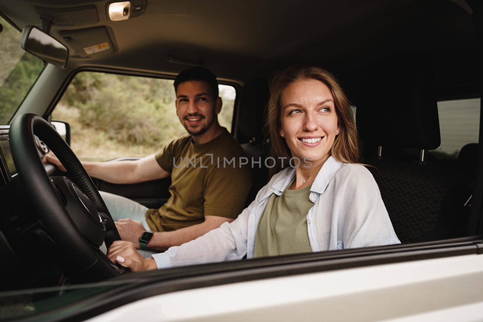 Beautiful young couple sitting on front passenger seats and driving a car by Fabrikasimf