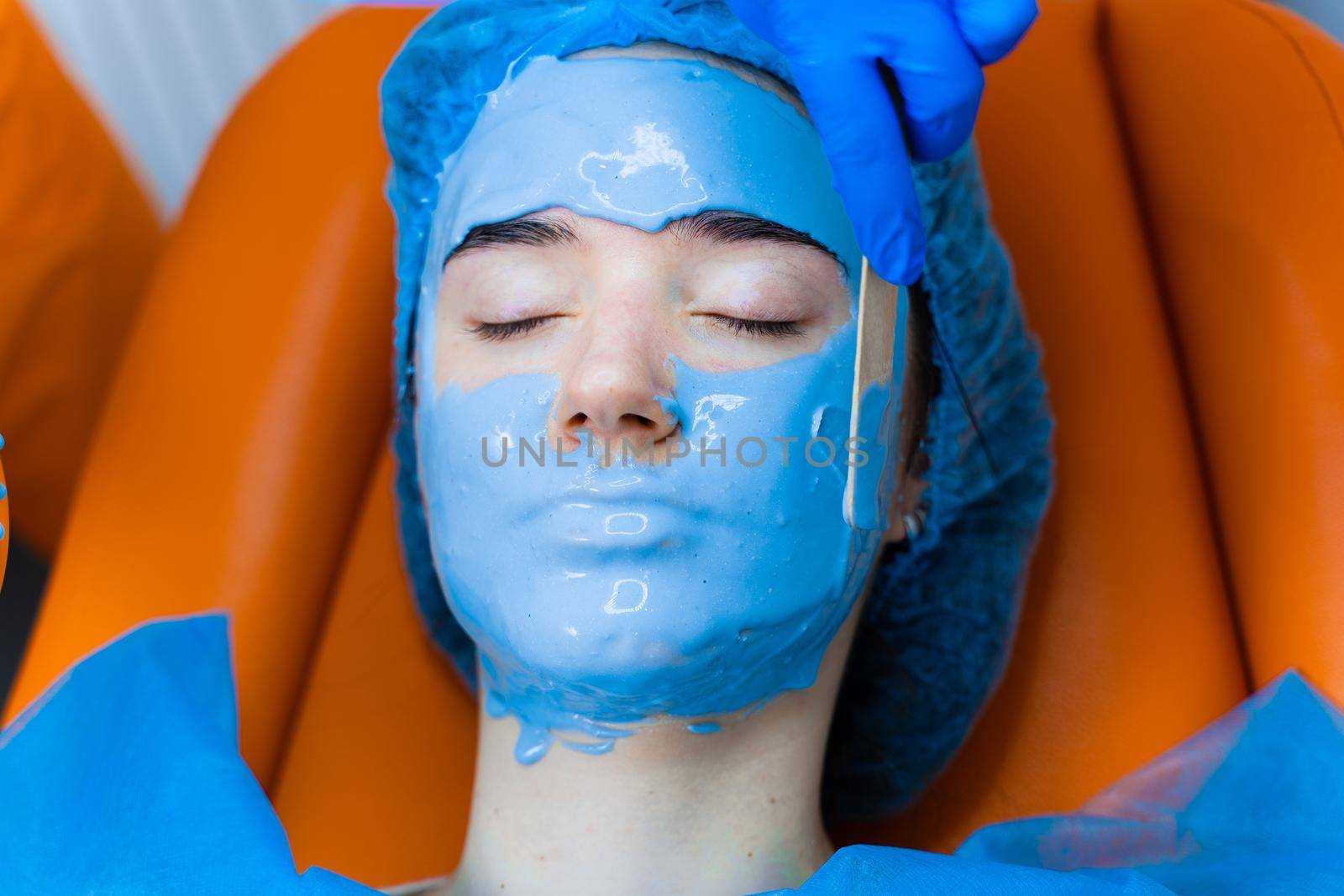 Alginate moisturizing mask for face and skin of young girl. Spa procedure for rejuvenation. beautician smears blue mask. Dermatology in medical clinic