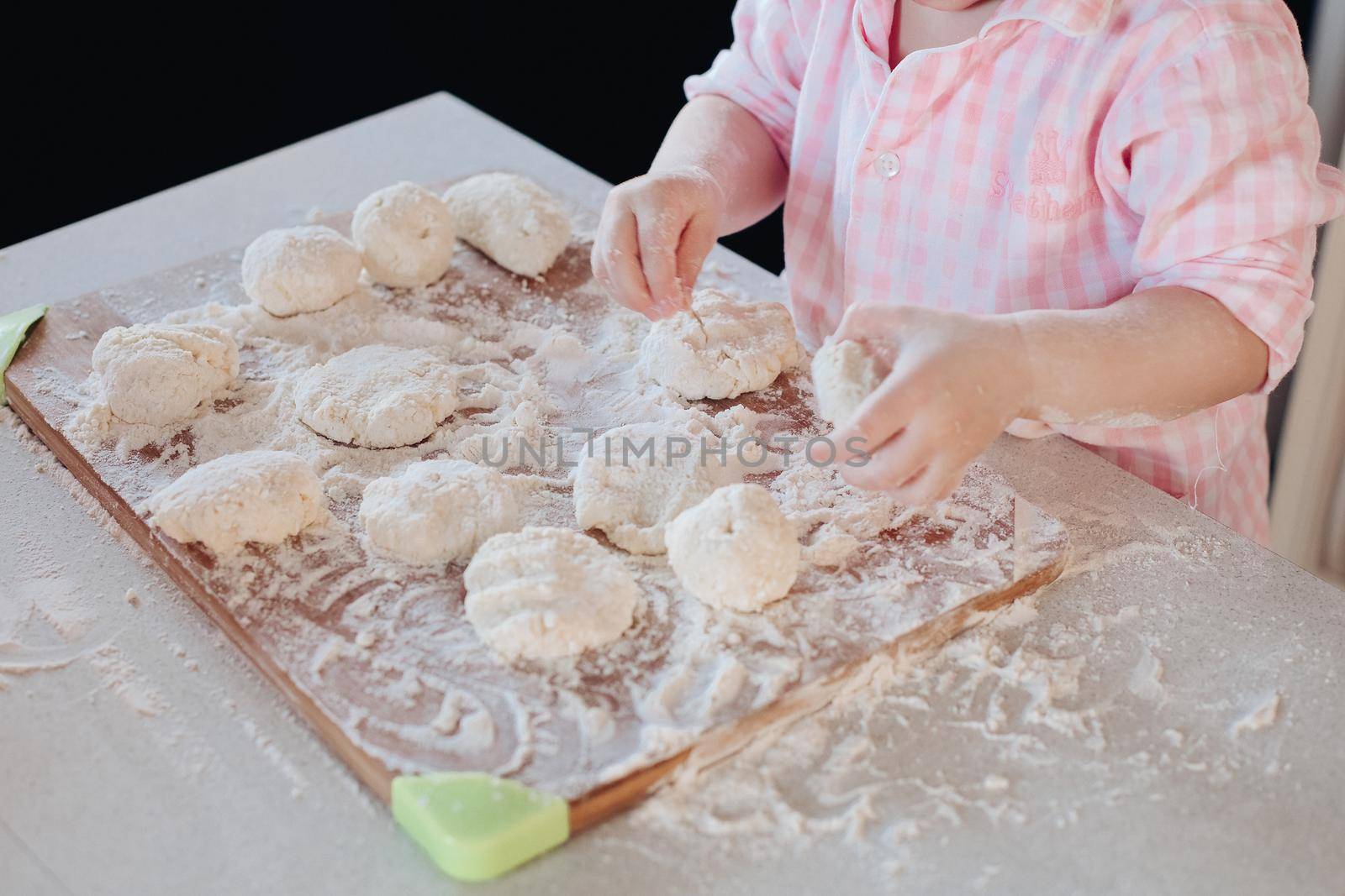 Little lovely kid helping parent with dough at kitchen. by StudioLucky