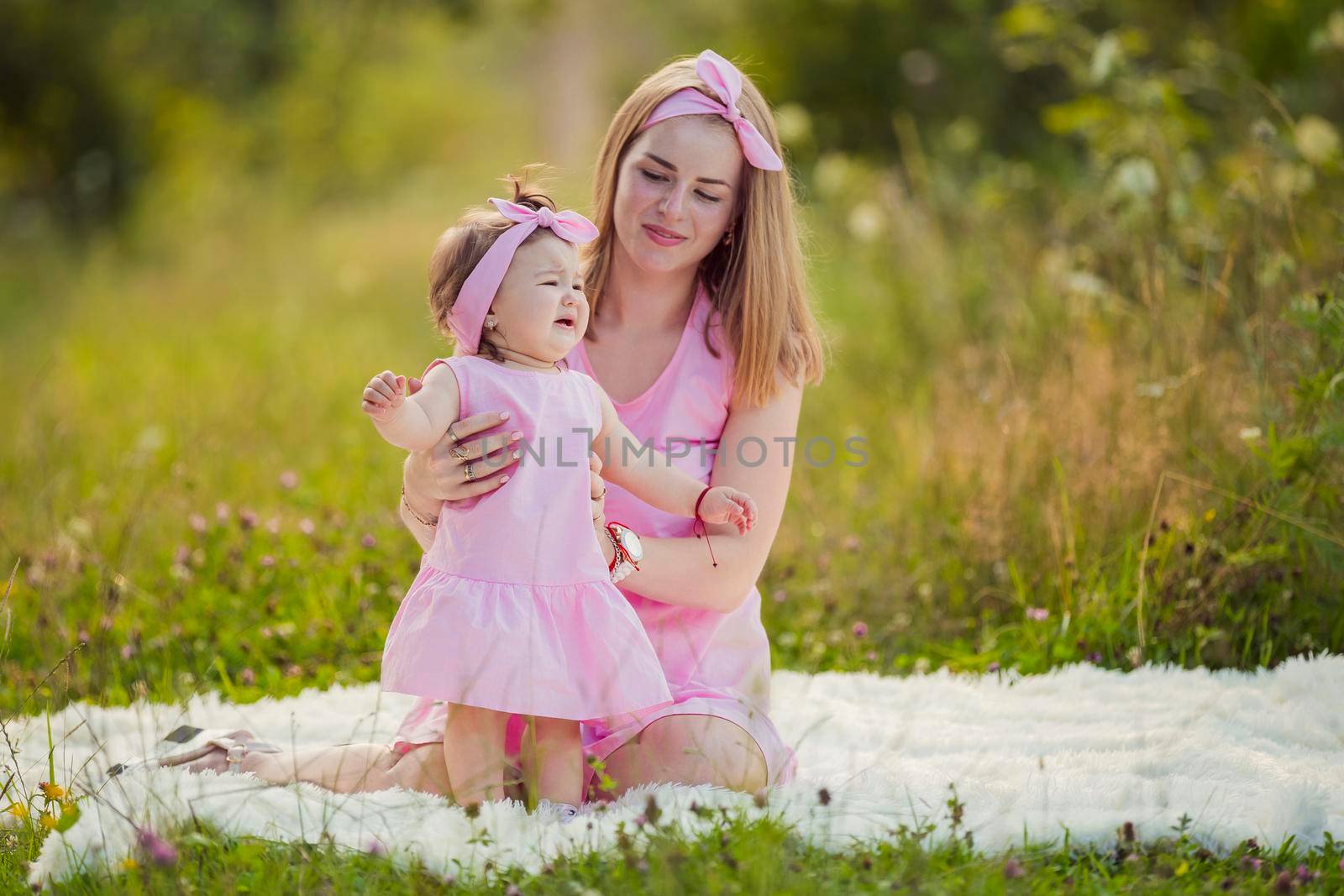 mother and daughter in identical pink dresses are sitting in nature