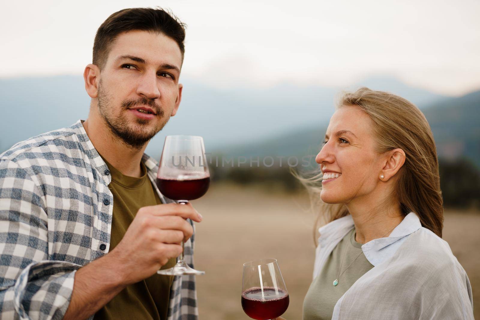 Smiling couple toasting wine glasses outdoors in mountains, close up portrait