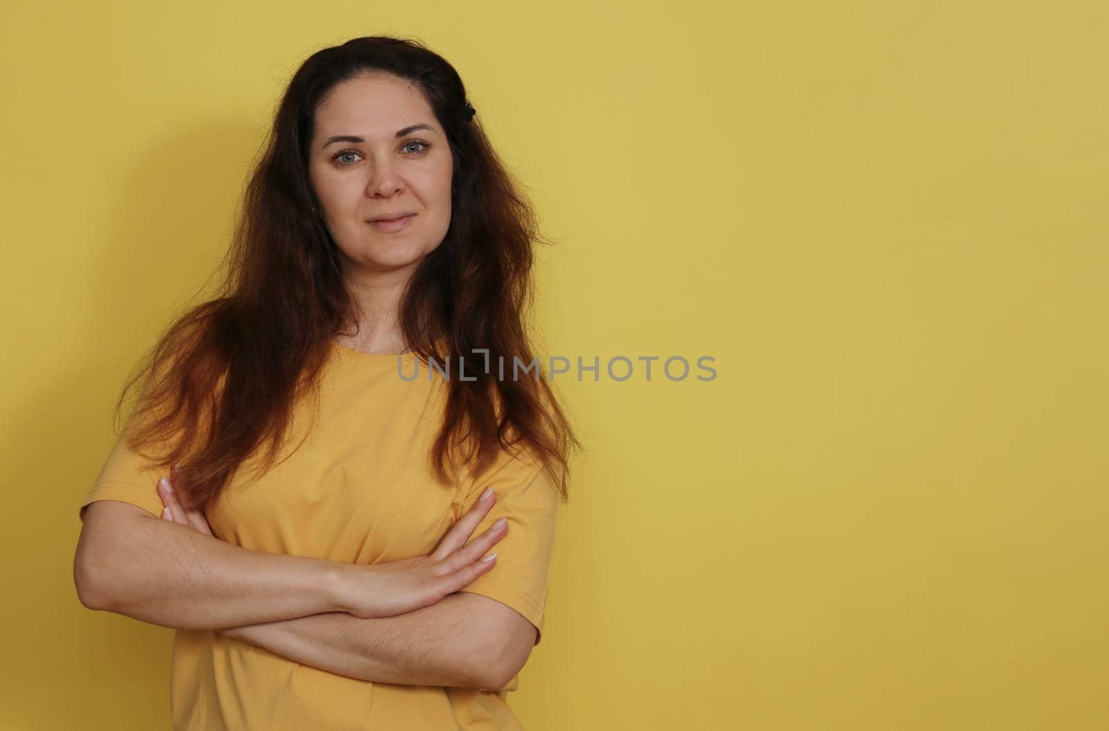Pretty brunette 30-35 yo smiles tenderly, dressed in casual clothes, expresses positive emotions. Beautiful woman in yellow t-shirt with long dark hair on yellow paper background.