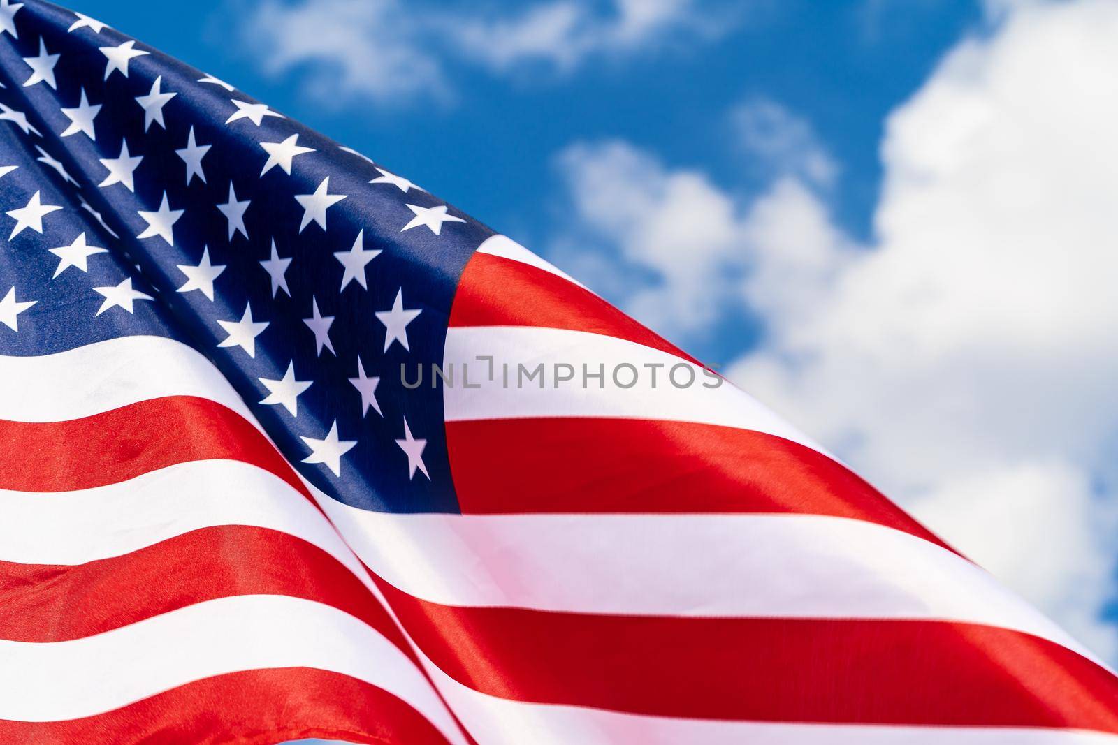 American flag on flagpole waving in the wind against white clouds