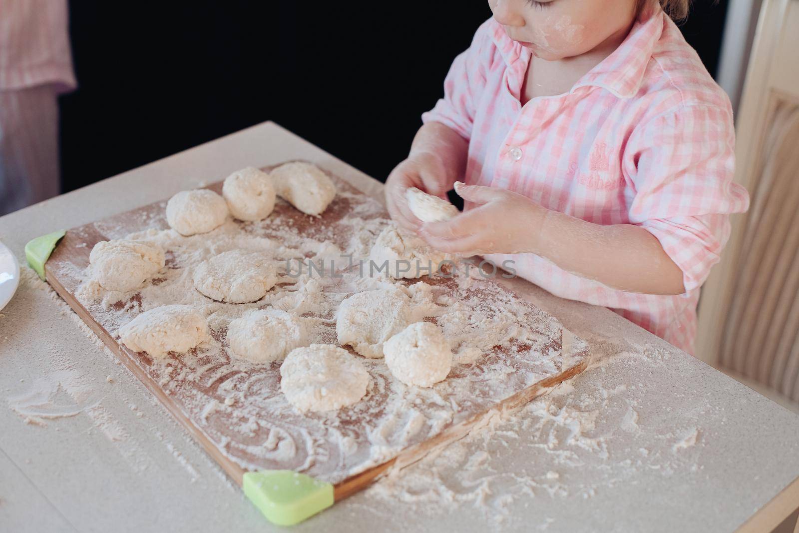 Little lovely kid helping parent with dough at kitchen. by StudioLucky