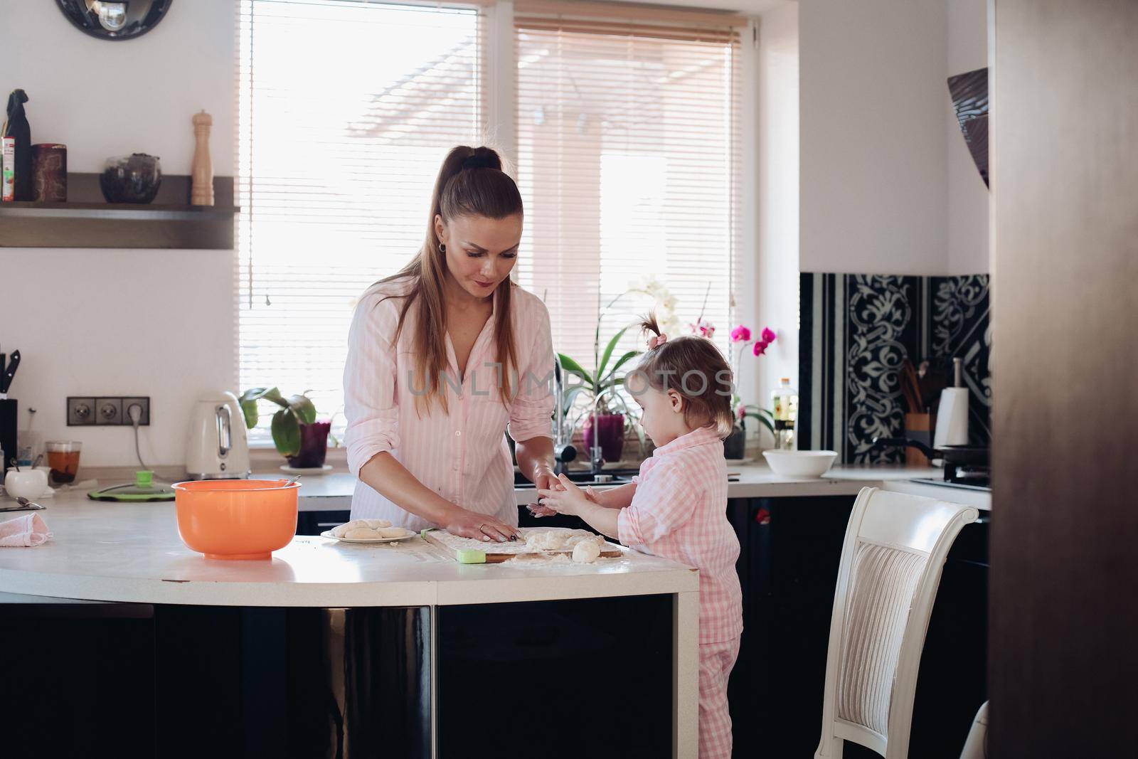 Lovely mother playing with little daughter in kitchen. Cheerful woman and cute girl cooking and baking donuts at kitchen. Happy family laughing and talking together at home. Concept of love and joy.