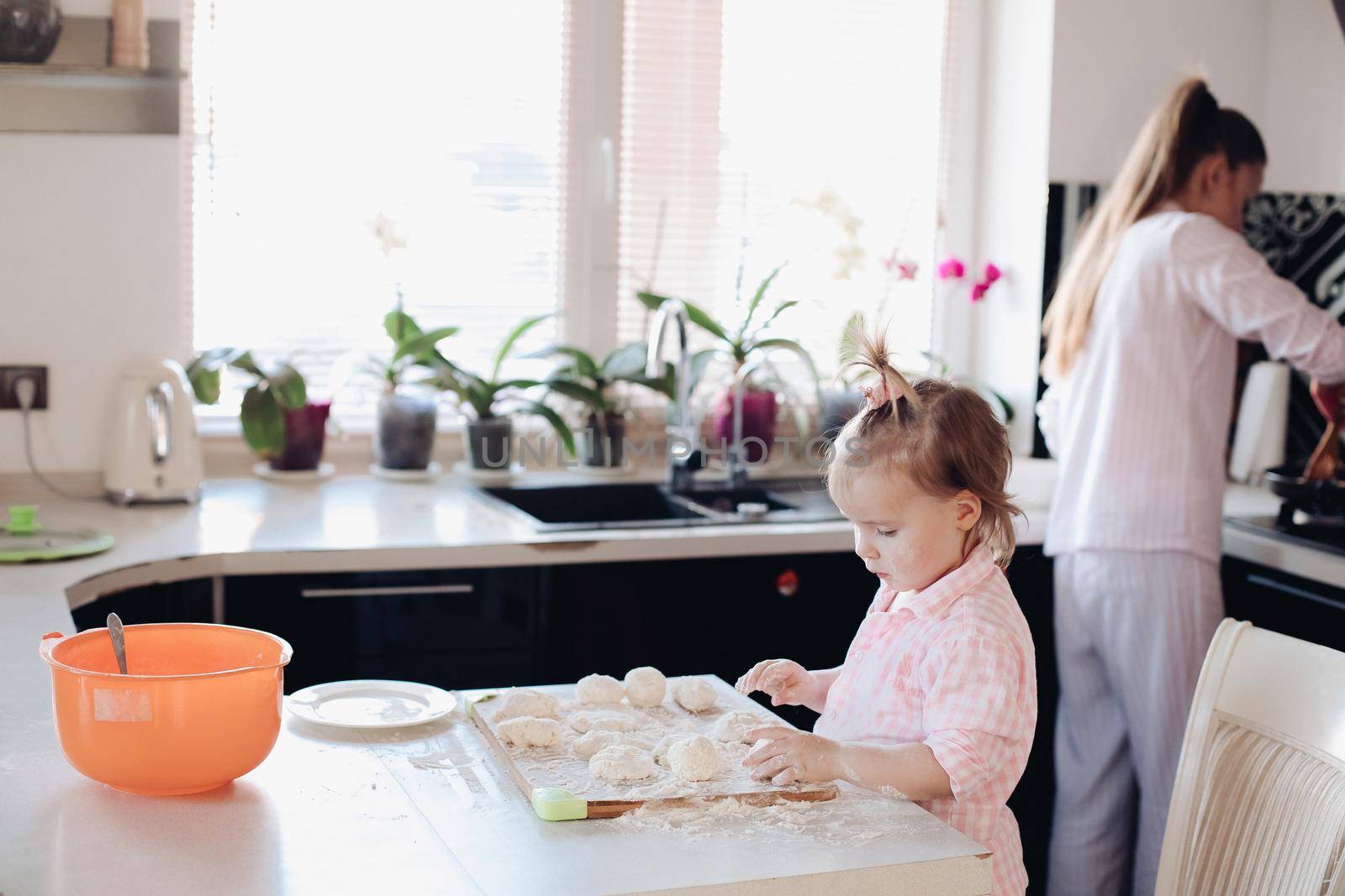 Happy wife smiling and preparing breakfast together with child for husband. Beautiful mother with cute daughter cooking in pajamas in morning. Little lovely kid helping parent with dough at kitchen.