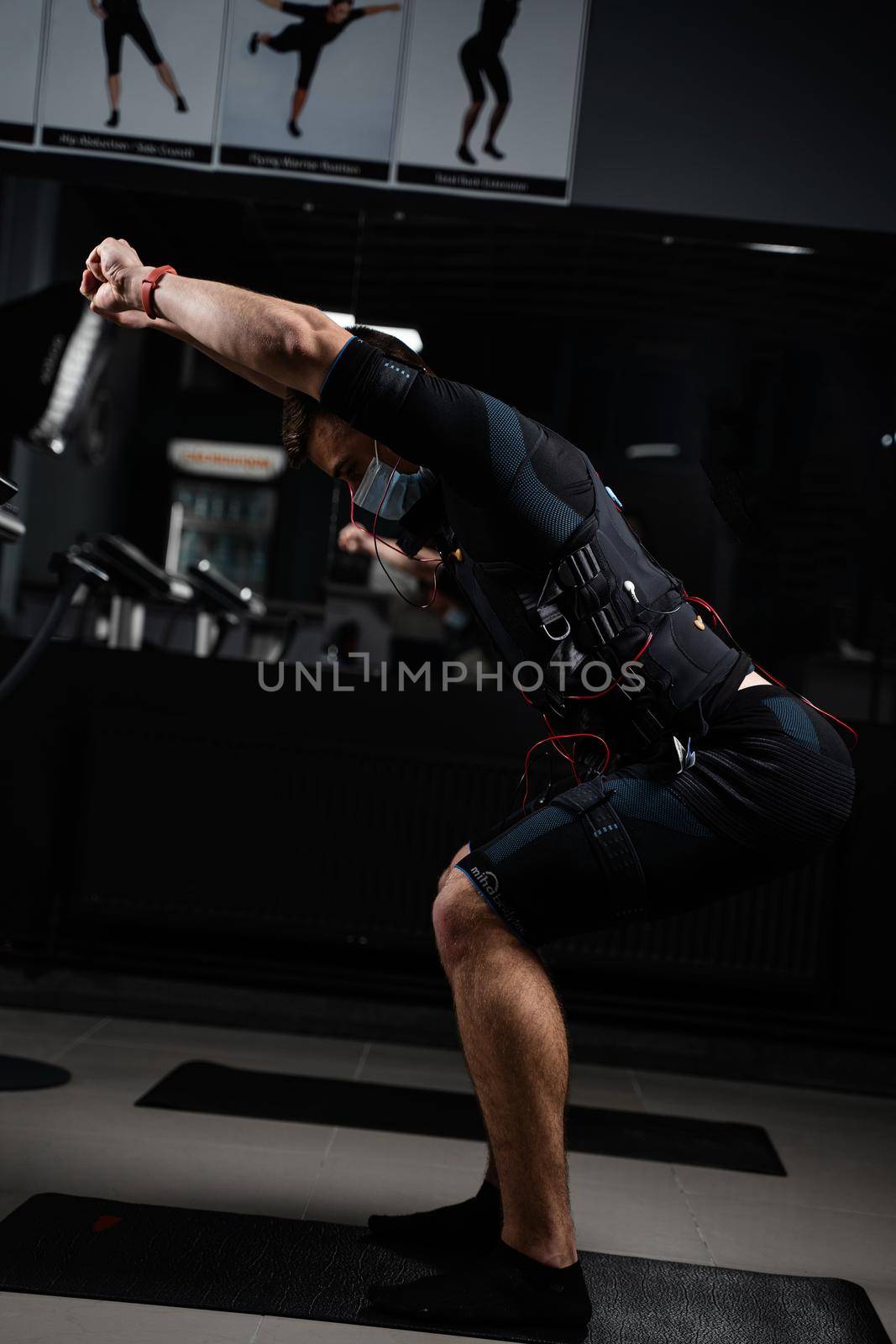 Man in EMS suit and medical mask in gym. Protection from coronavirus covid-19. Sport training in electrical muscle stimulation suit at quarantine period