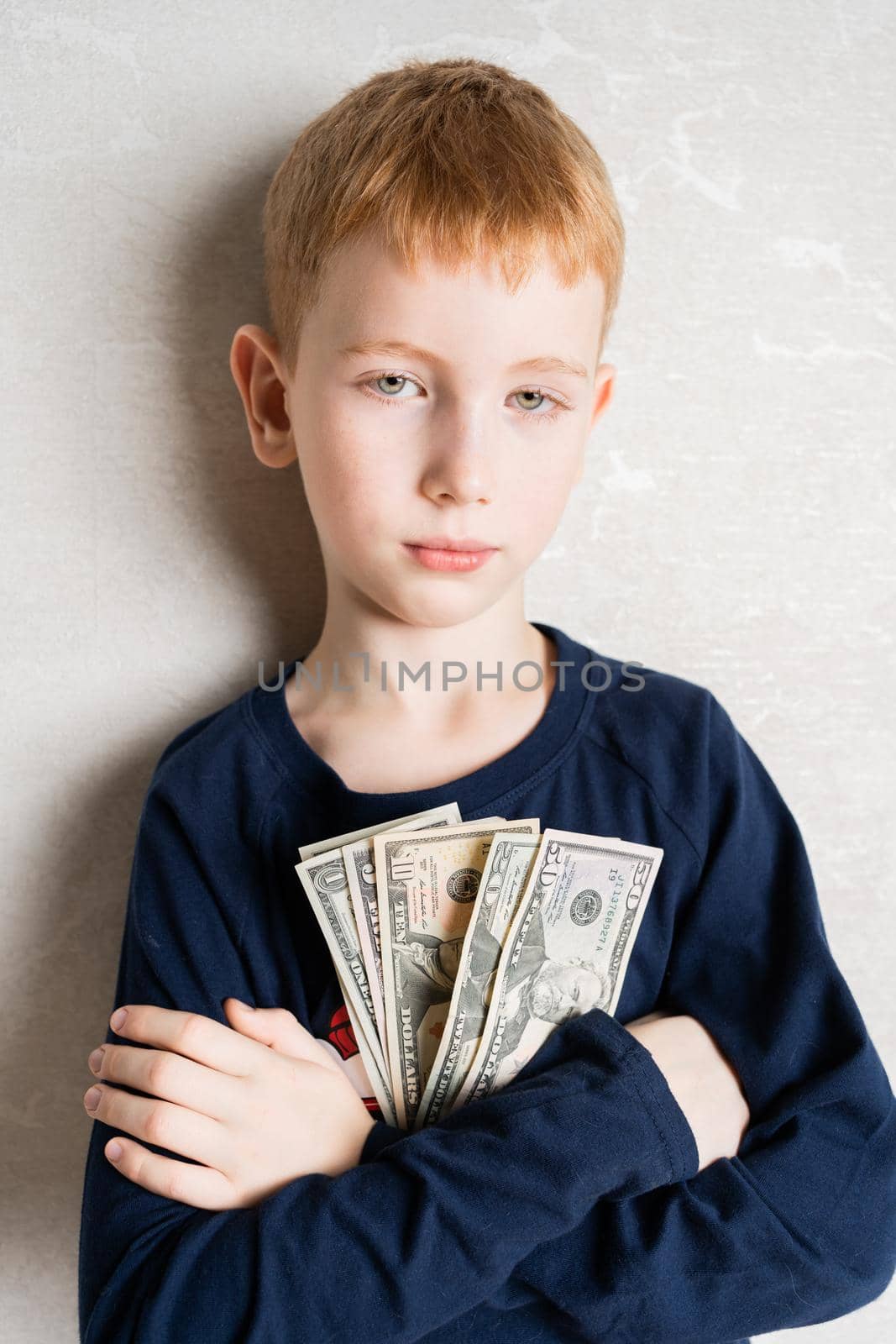 a red-haired boy, with his arms crossed on his chest, holds in his hands the first money earned, dollars. The look of a self-confident person looking at others from a high