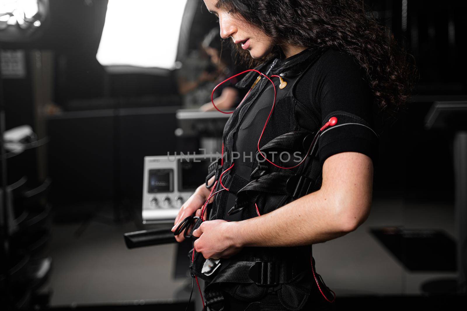 Girl in EMS suit in gym. Sport training in electrical muscle stimulation suit. Making physical exercises.