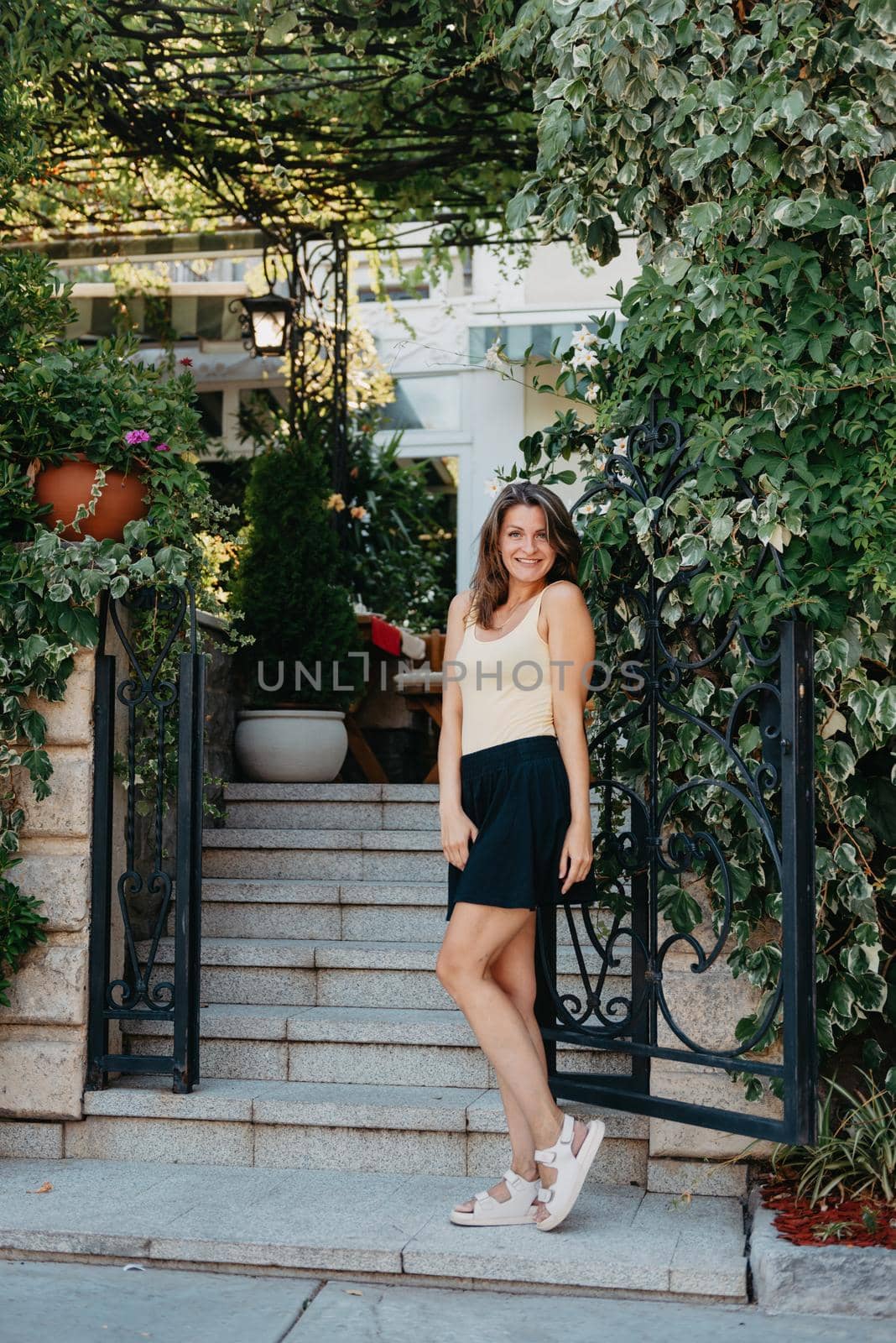 Girl tourist walking through ancient narrow street on a beautiful summer day in MEDITERRANEAN MEDIEVAL CITY , OLD TOWN bUDVA, MONTENEGRO. Young beautiful cheerful woman walking on old street at tropical town. Pretty girl looking at you and smiling