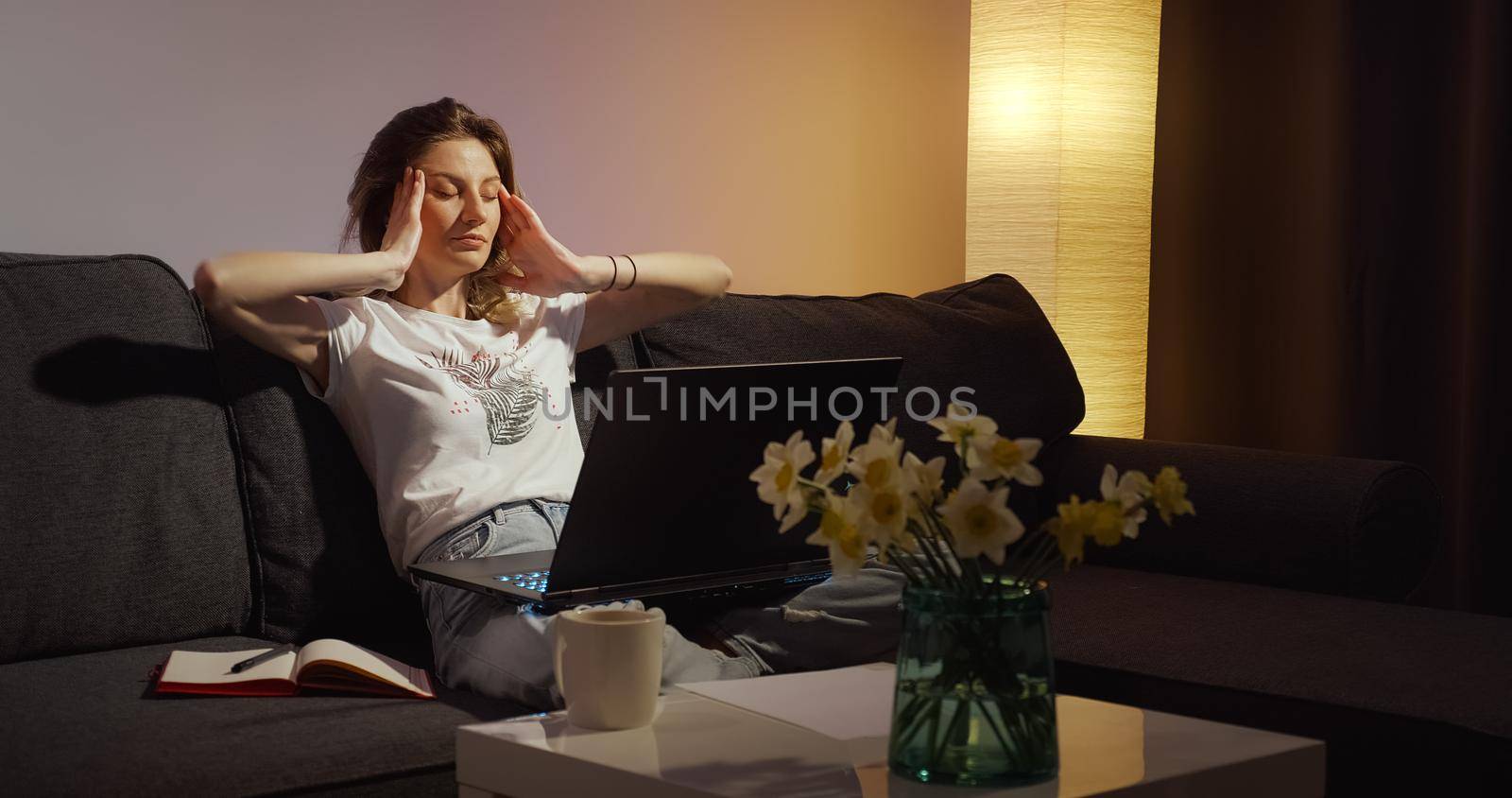 Young woman working on laptop alone in dark living late at night finishing urgent work overworking.