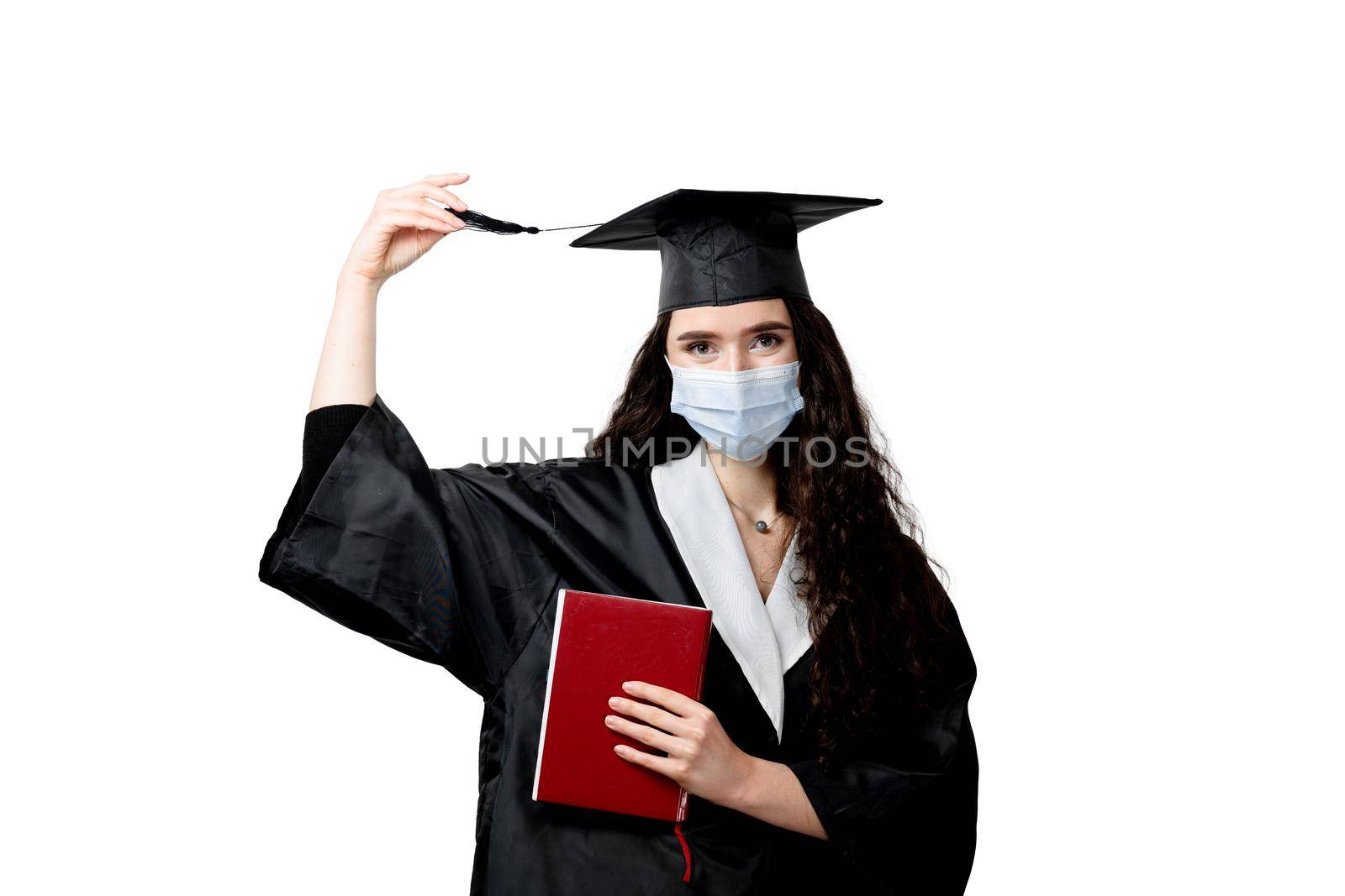 Student with book in graduation robe and cap in medical mask at coronavirus covid-19 period. Future leader of science. Academician young woman in black gown smiling.