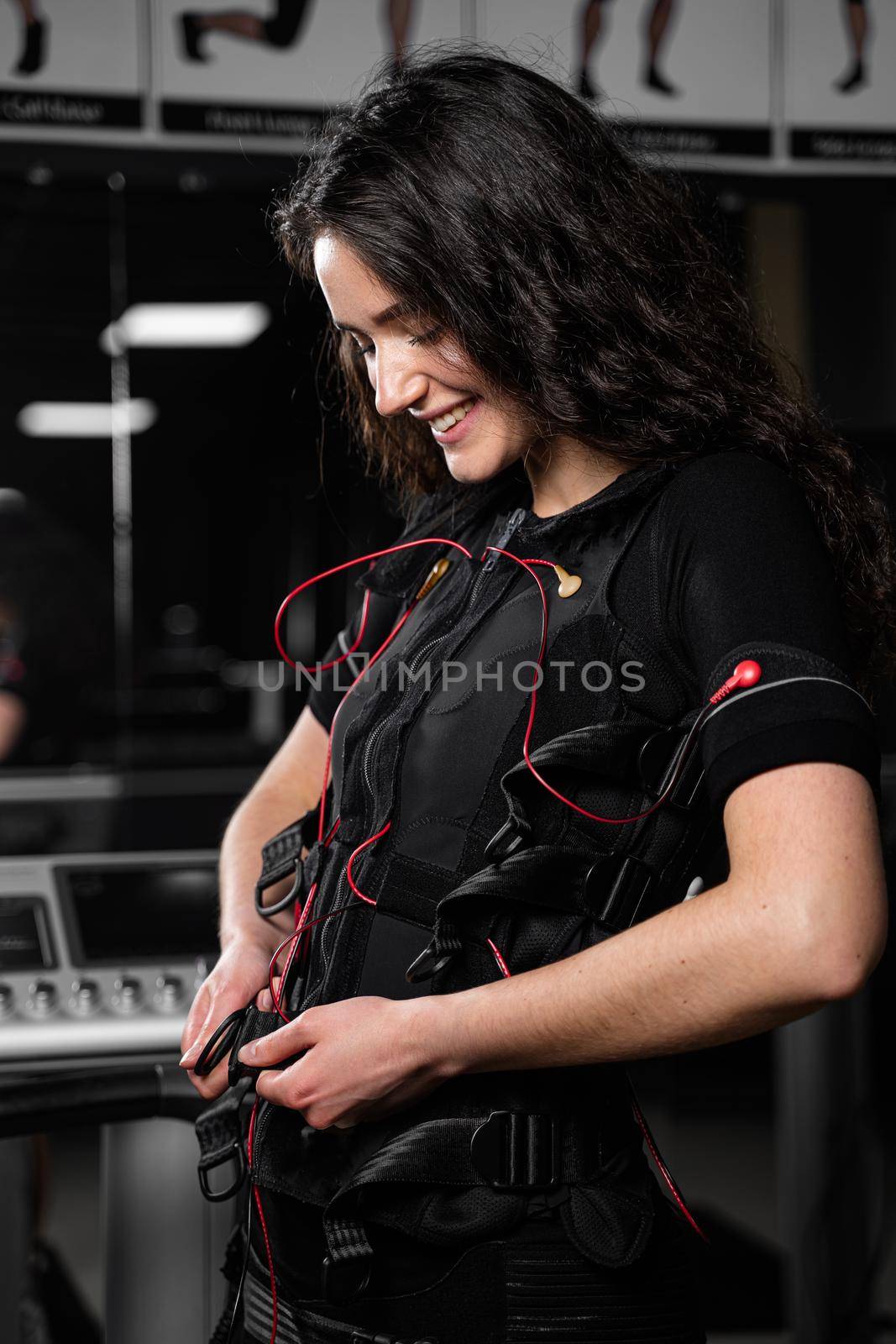 Girl in EMS suit in gym. Sport training in electrical muscle stimulation suit. Making physical exercises.