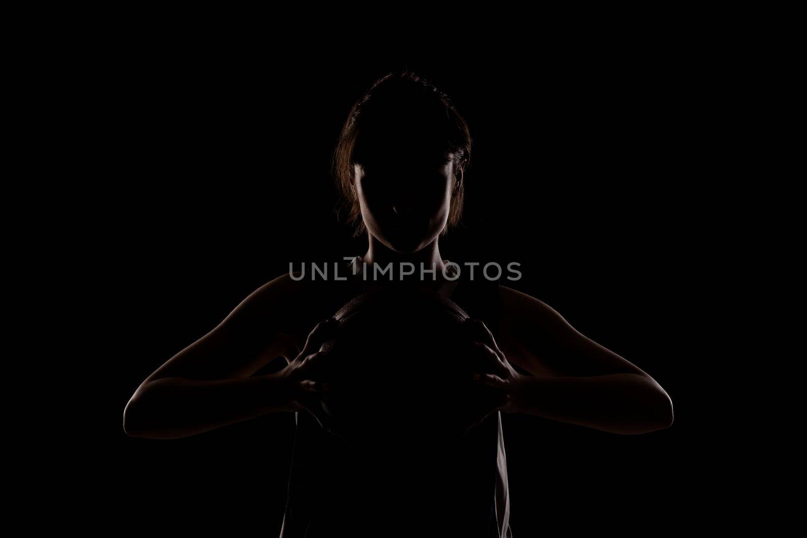 Female basketball player. Beautiful girl holding ball. Side lit silhouette studio portrait against black background.