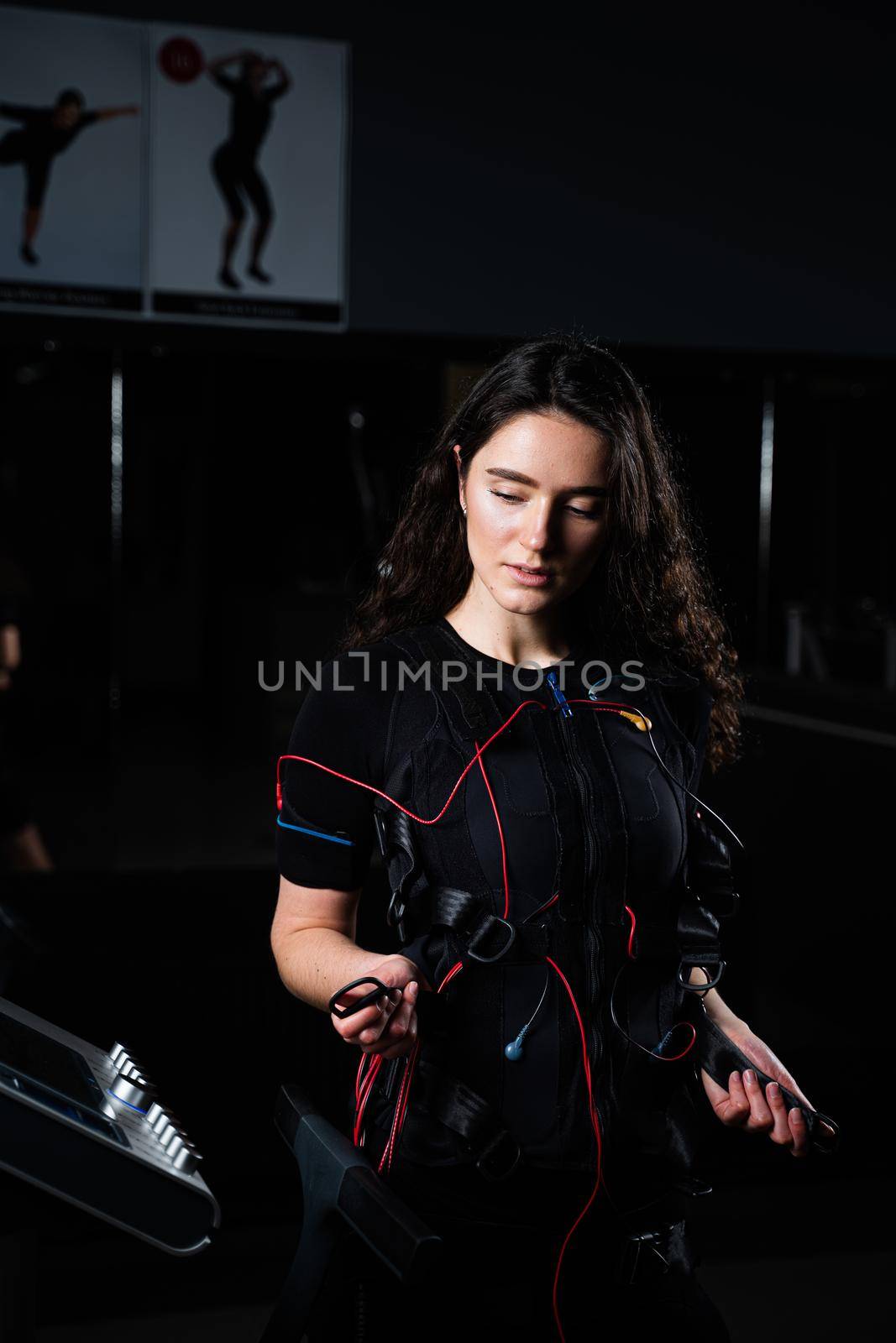 Girl in EMS suit in gym. Sport training in electrical muscle stimulation suit. Making physical exercises by Rabizo