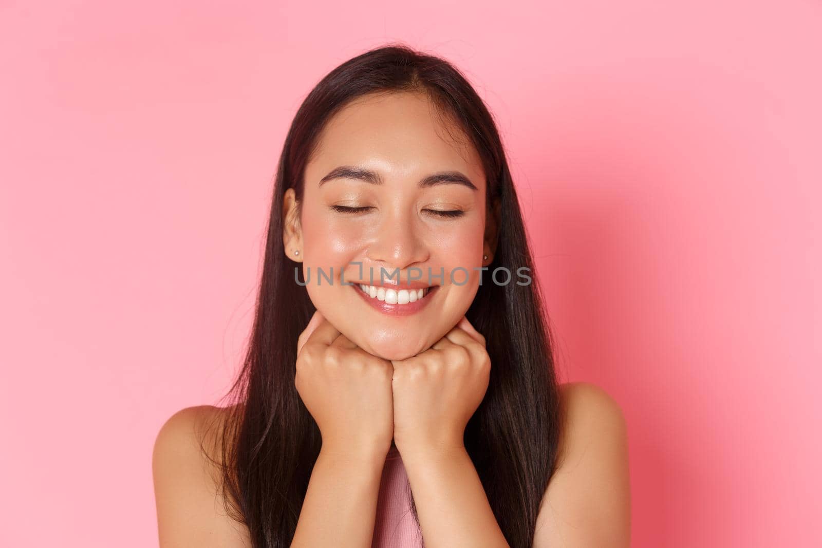 Beauty, fashion and lifestyle concept. Close-up of dreamy and romantic, attractive asian girl daydreaming, leaning face on hands and close eyes with happy white smile, pink background by Benzoix