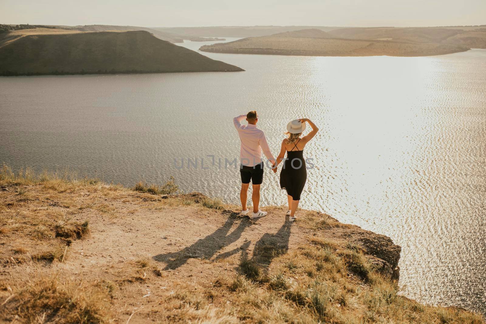 A man and a woman in love walk on a mountain above a large lake by the sea at sunset. A couple of fair-haired fair-skinned people in love are resting in nature in a field