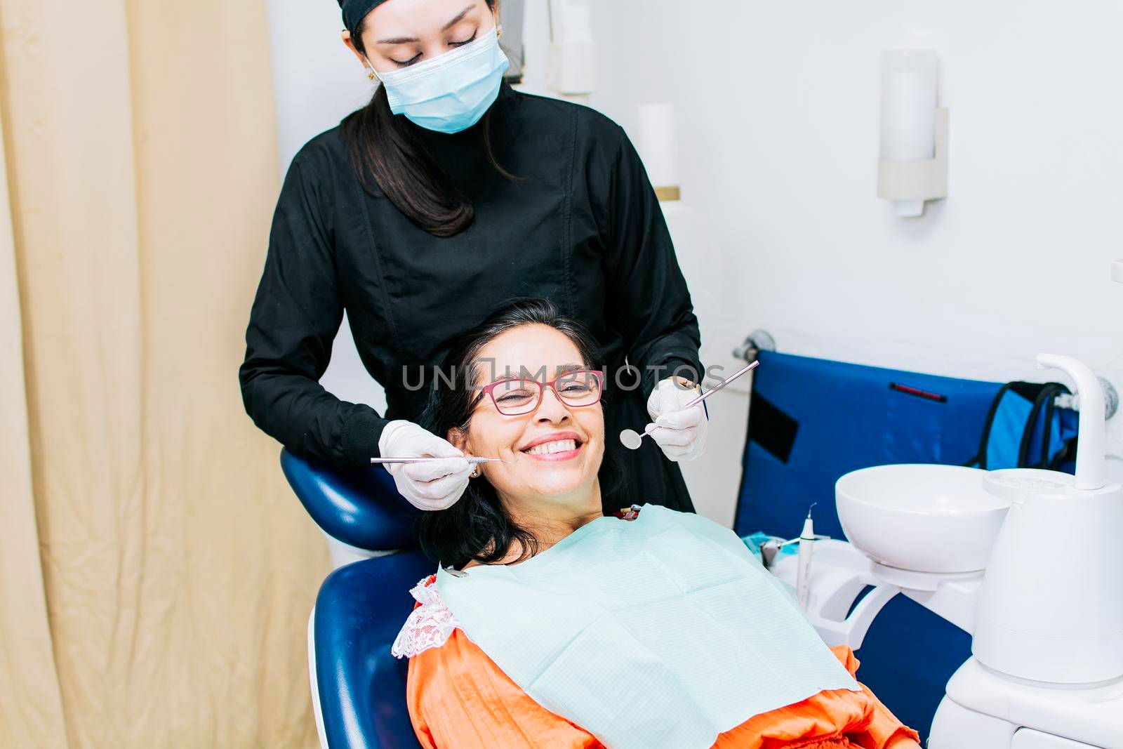 Dentist examining mouth to smiling patient, Female dentist doing root canal to female patient, Female dentist with lying patient, Dentist performing stomatology by isaiphoto