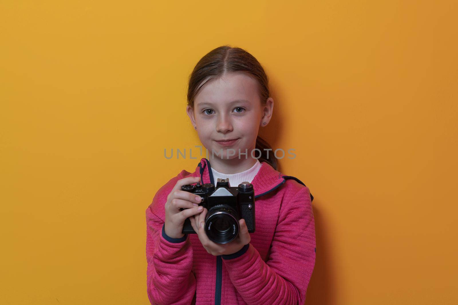 Little girl photographer isolated on yellow background smiling taking photos with a retro vintage camera. High quality photo