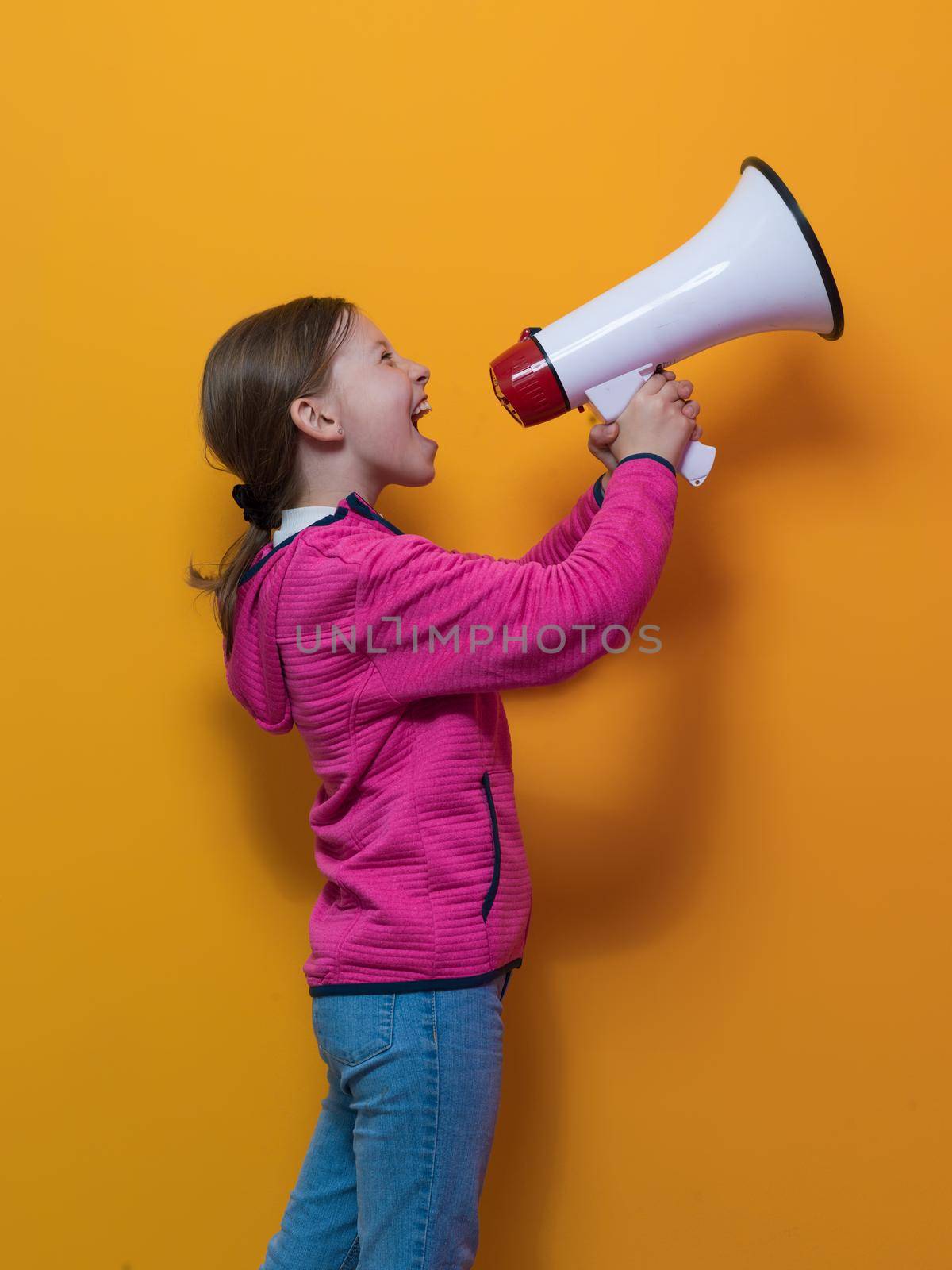 Funny little kid girl Screaming in megaphone over the yellow background in studio. People sincere emotions lifestyle concept. Mock up copy space. High quality photo