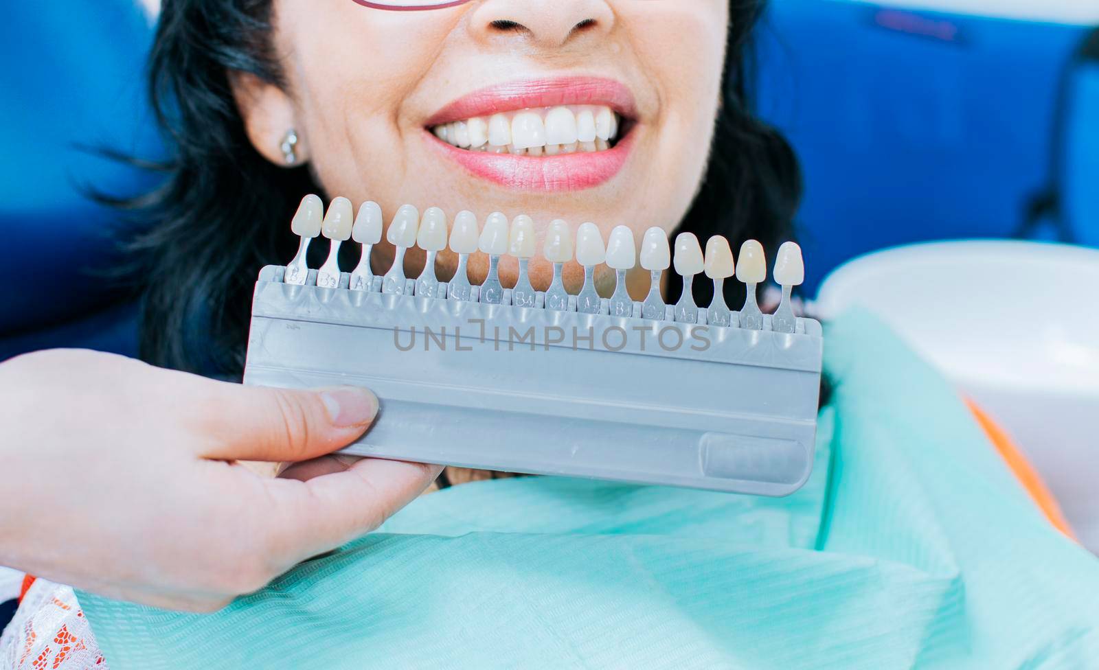 Cosmetological teeth whitening in a dental clinic, selection of the tone of the implant tooth, Woman Holding Set Of Implants With Various Shades Of Tone, Smiling young woman.  by isaiphoto
