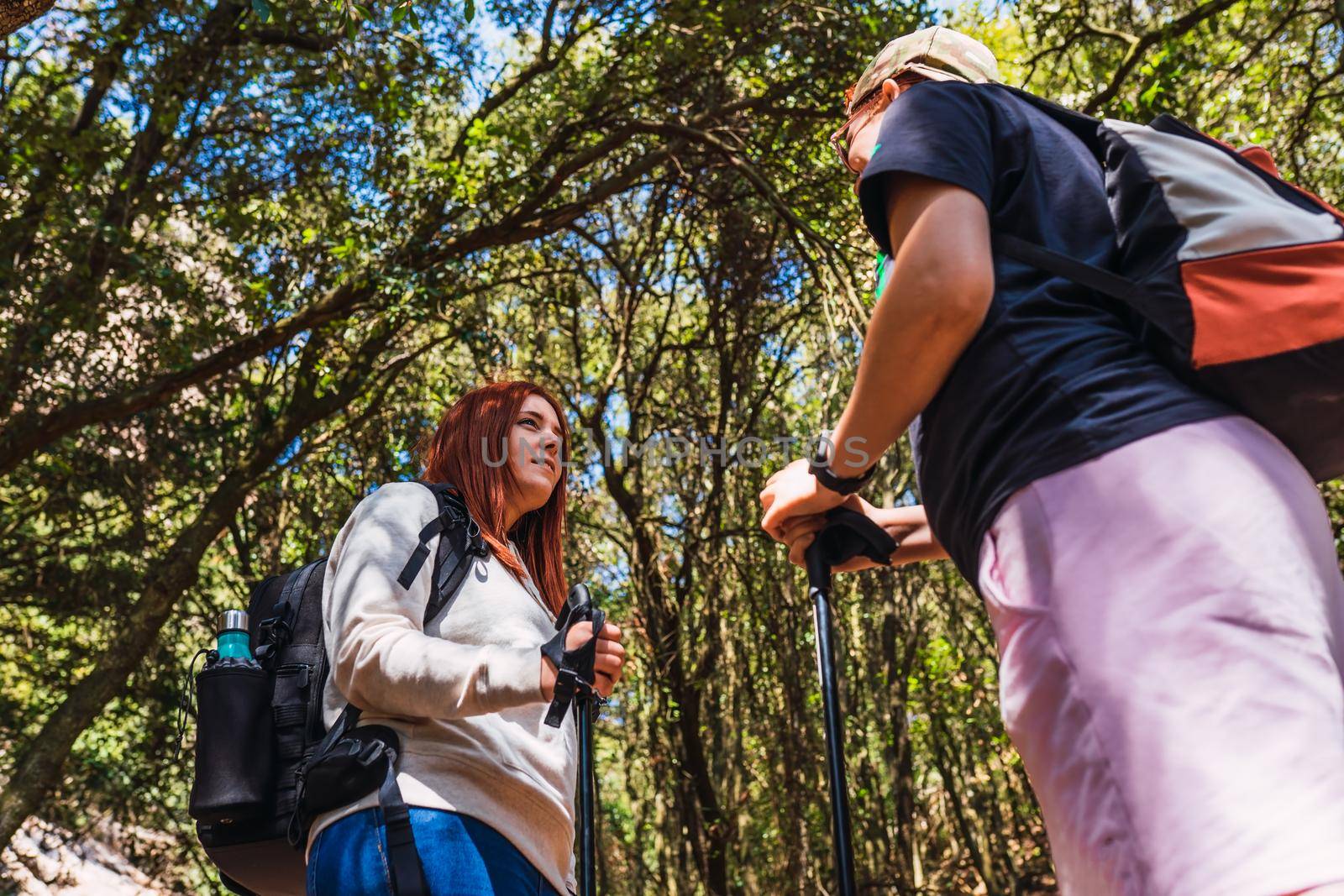 young women relaxing and enjoying themselves on a mountain trail. tourists hiking in nature. young people on holiday. hiking poles and mountaineer's backpack. natural and warm light. lush vegetation. hiking poles.