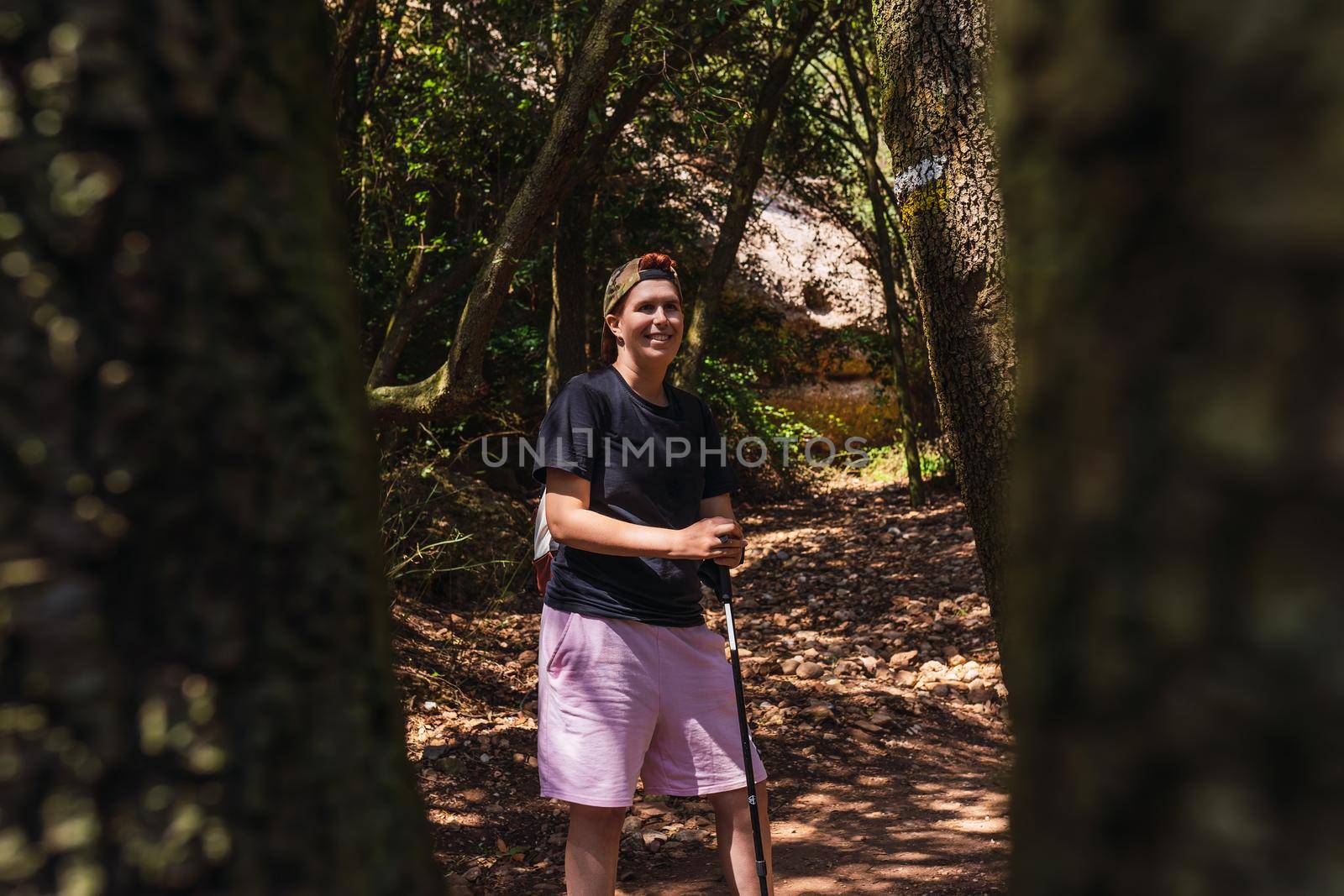 young woman hiking on a forest track. enjoying her holiday. woman walking in nature. hiking poles and mountaineer backpack. natural and warm light. lush vegetation. hiking poles.