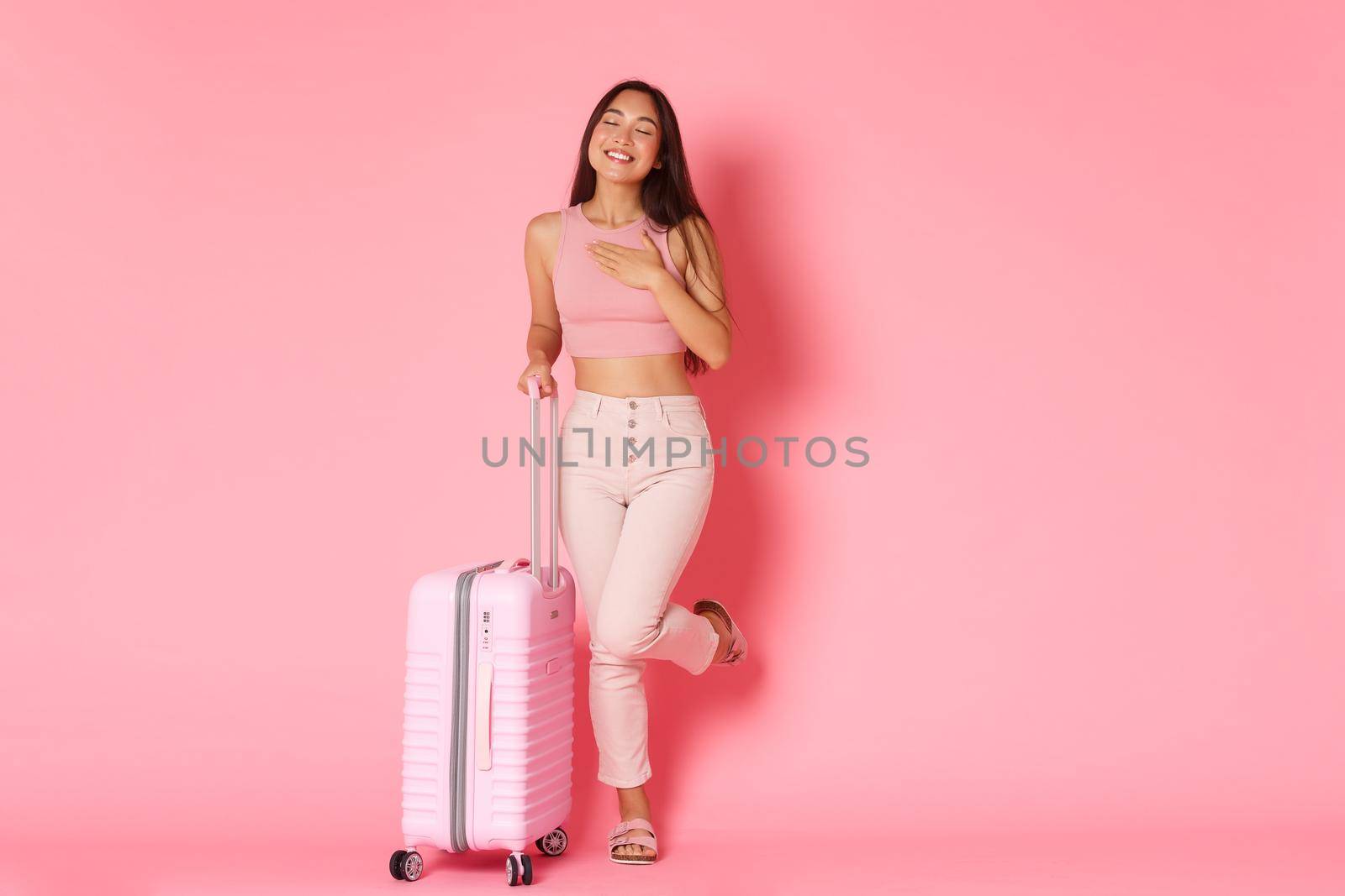 Travelling, holidays and vacation concept. Full-length of dreamy, silly asian girl daydreamign about future travel, tourist dreaming about paradise resort, standing with suitcase, pink background by Benzoix