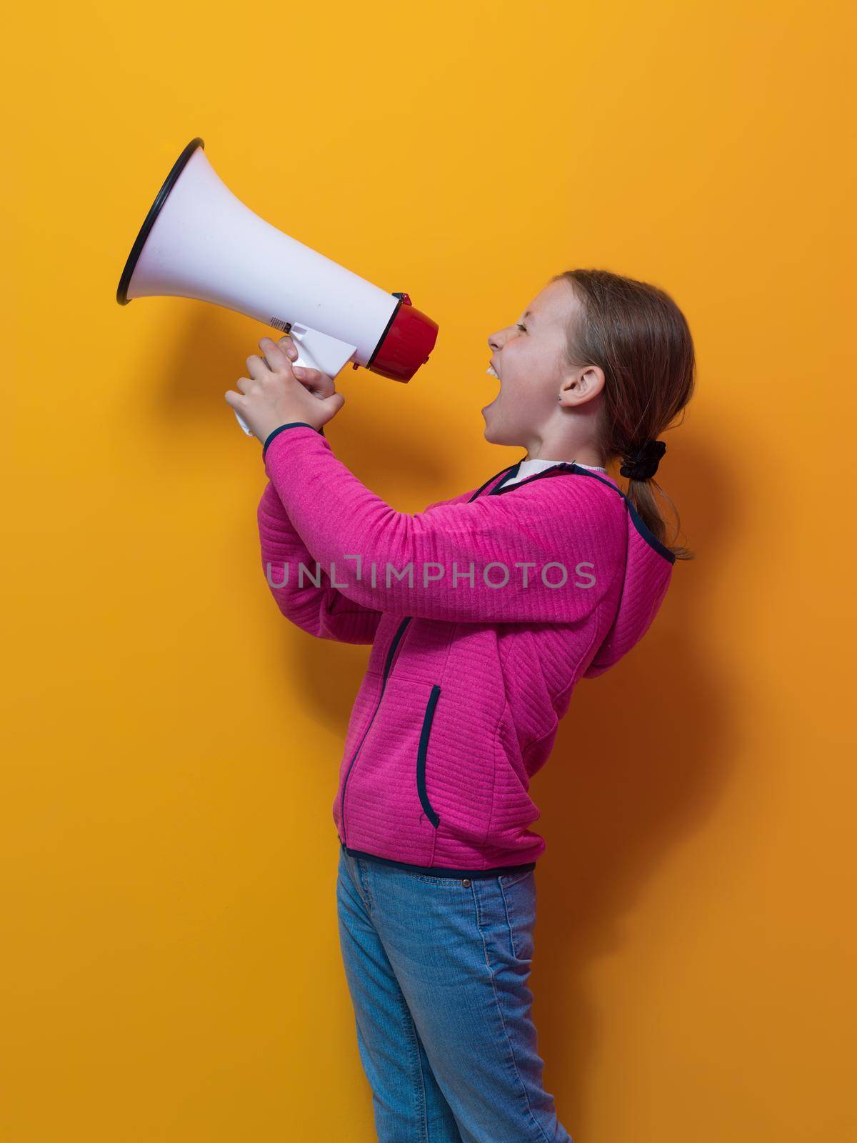 Funny little kid girl Screaming in megaphone over the yellow background in studio. People sincere emotions lifestyle concept. Mock up copy space. High quality photo