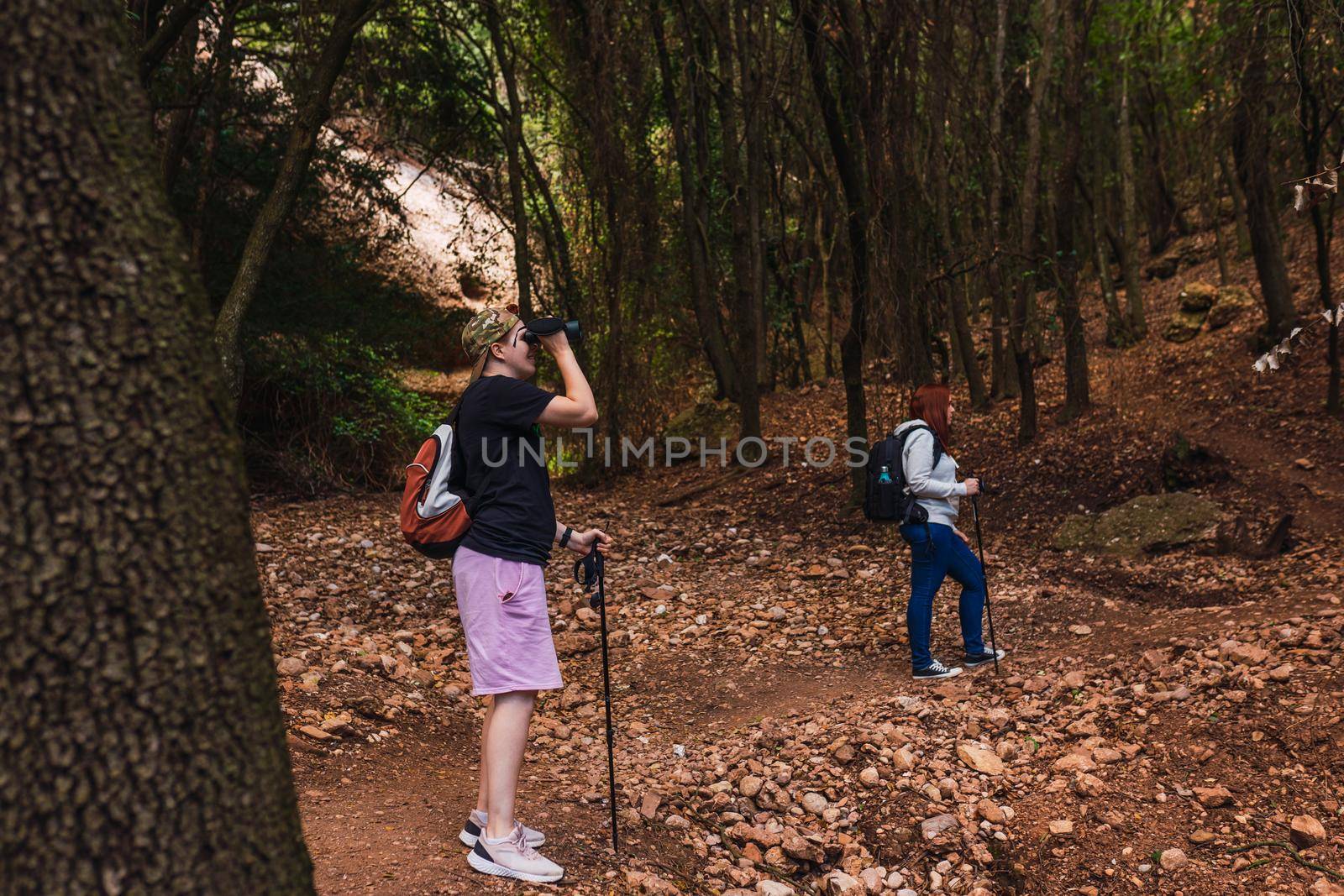 two friends climbing to the top of a mountain. young women on vacation. women using binoculars,bird watching. hiking sticks and mountaineer's backpack. warm, natural light. lush vegetation. hiking sticks.