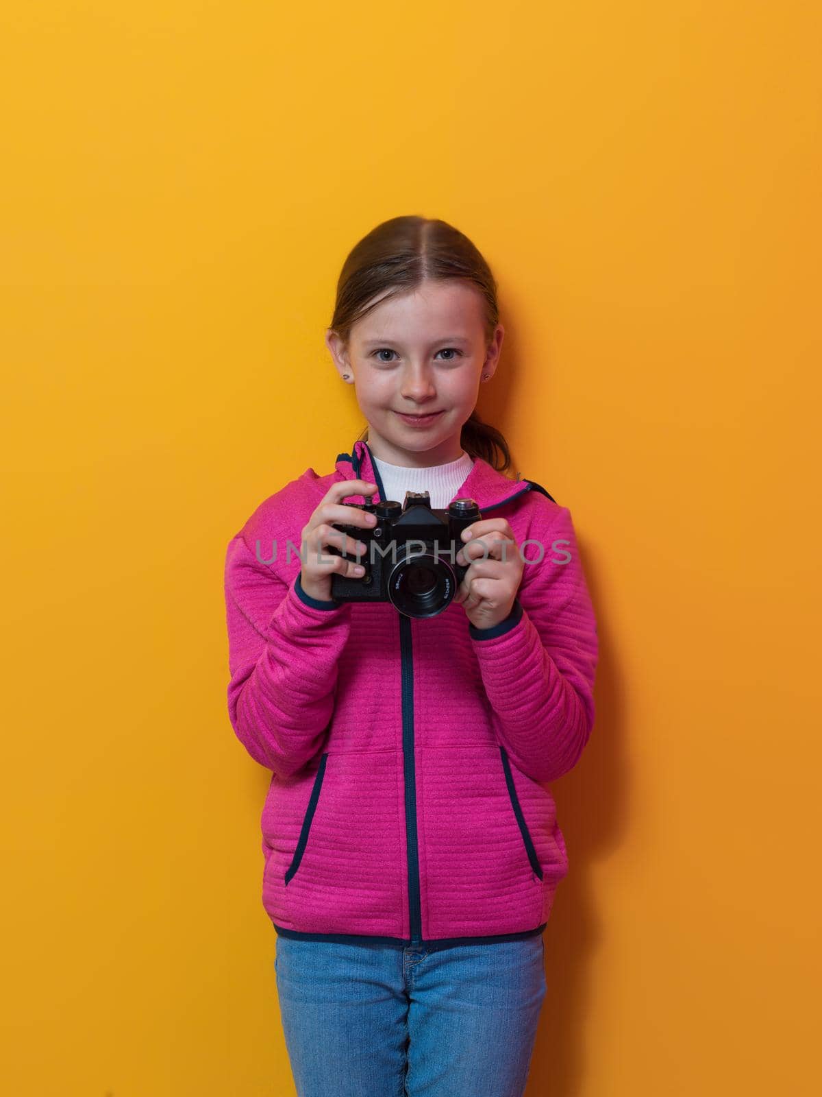 Little girl photographer isolated on yellow background smiling taking photos with a retro vintage camera. High quality photo