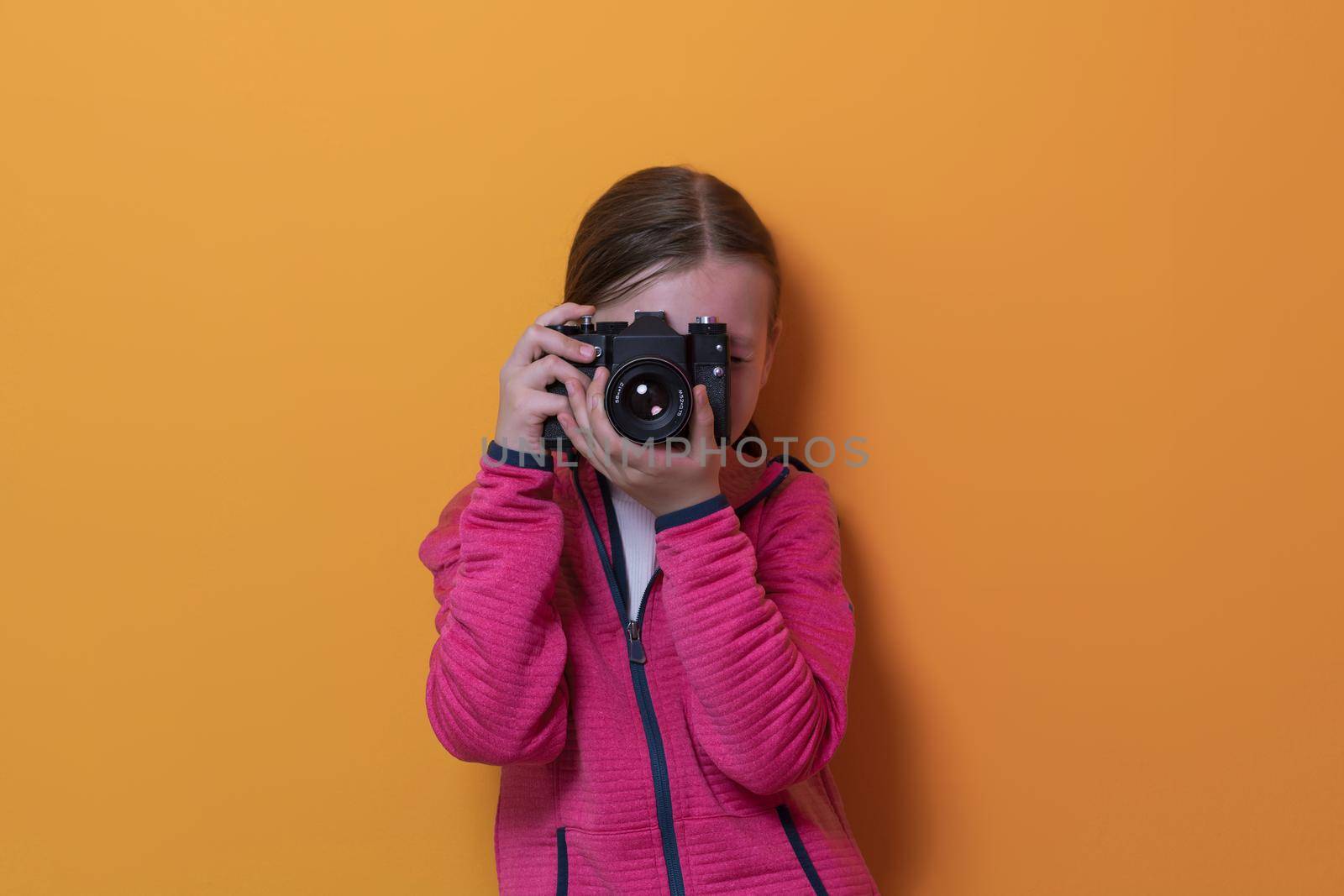 Little girl photographer isolated on yellow background smiling taking photos with a retro vintage camera. High quality photo