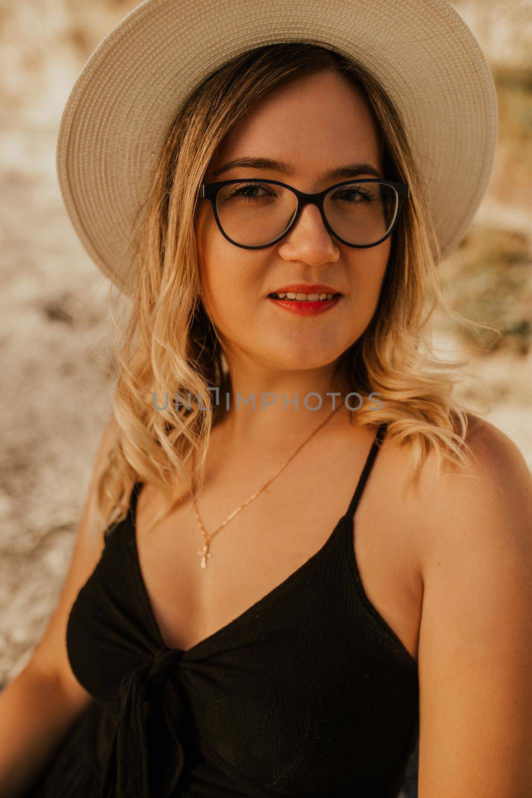 Light-skinned woman in glasses and a hat against background of a stone rock.