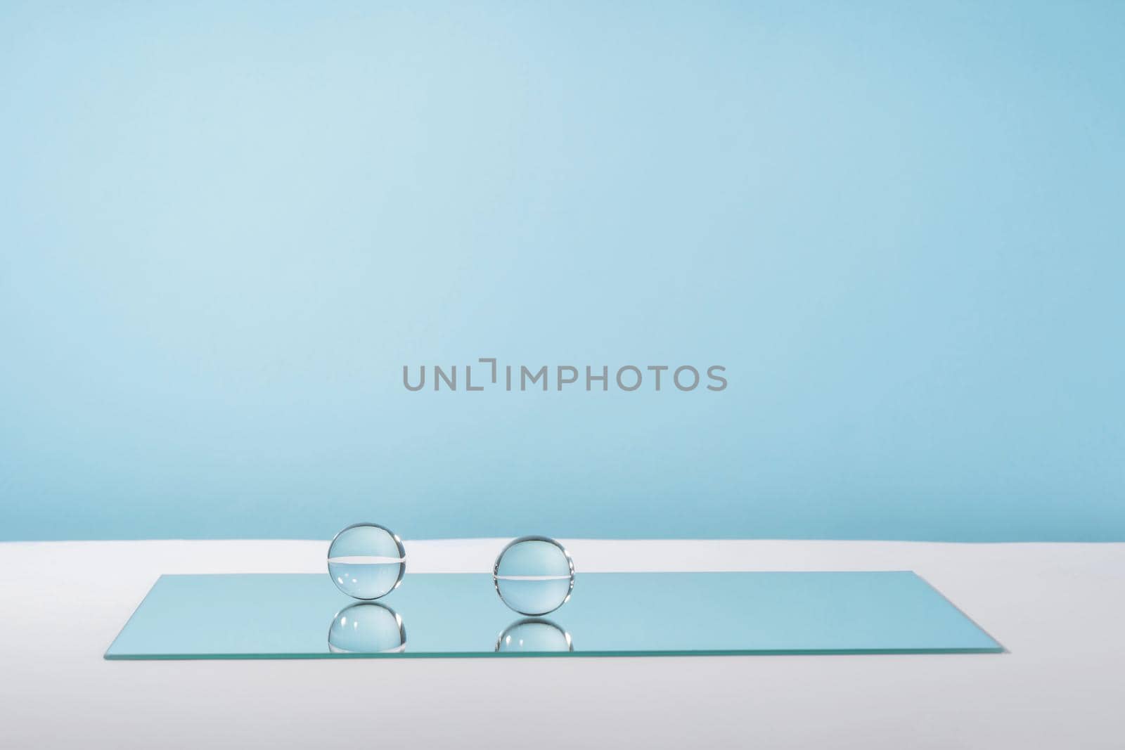 Pedestal cosmetic display glass podium platform with stylish props for product presentation, cosmetics geometric stand, mockup scene for jewellery. Balls and mirror on blue by photolime