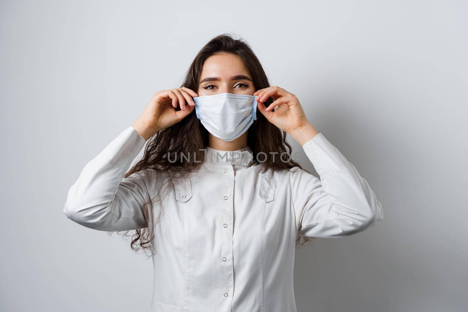 Doctor wearing medical mask on white background. Young attractive woman in medical robe. Quarantine coronavirus covid-19 trends.