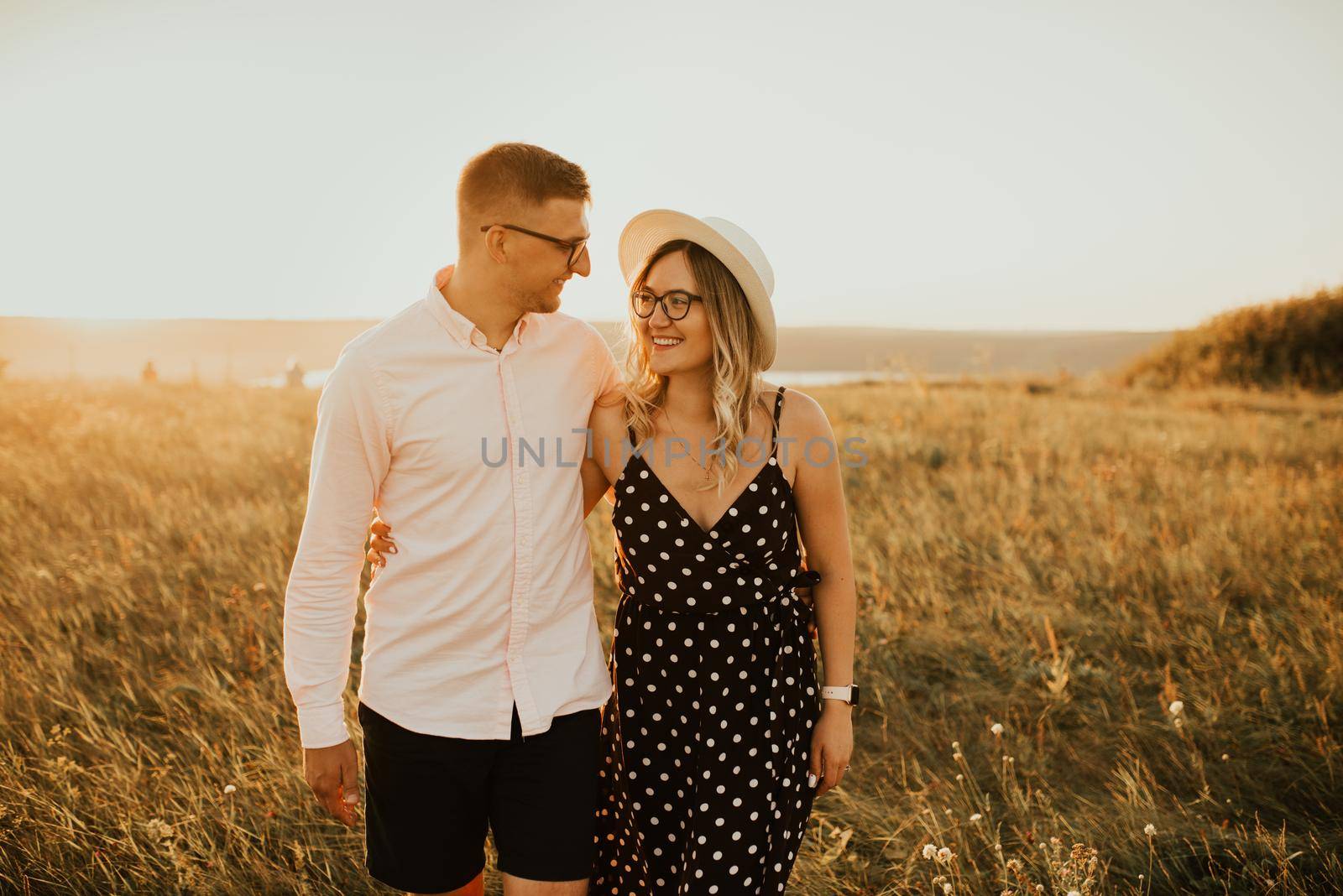 guy with a girl in hat walking in meadow by AndriiDrachuk