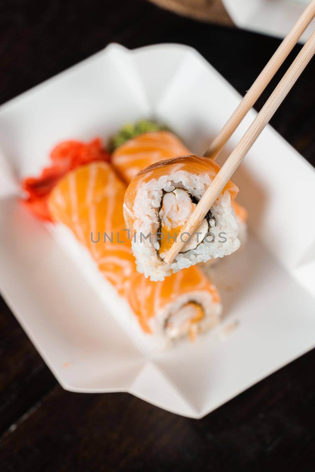 Holding philadelphia roll using chopstics for sushi. Roll with salmon, shrimp and mango. Japanese food delivery