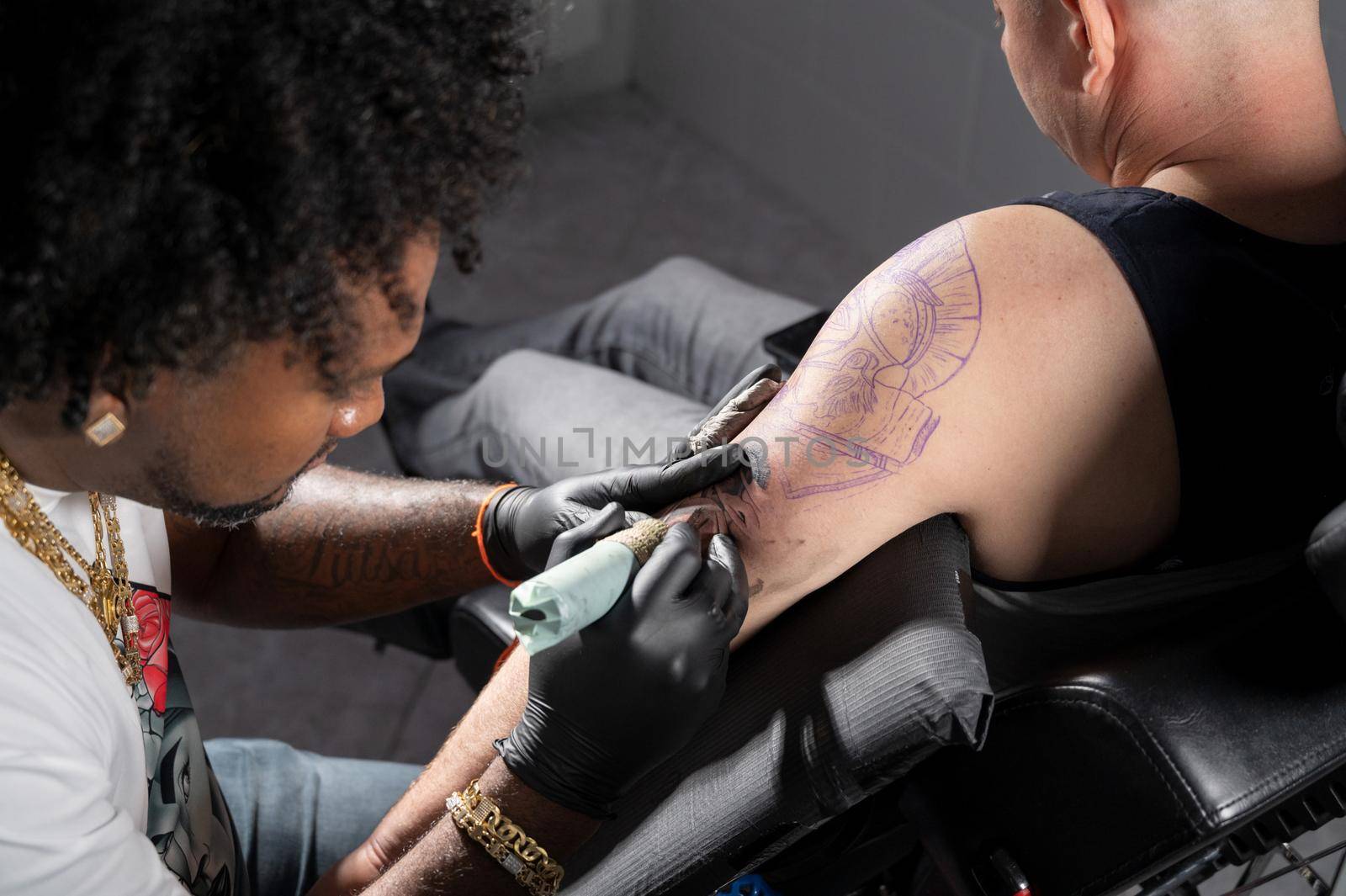 Professional African American tattoo artist makes a tattoo on client arm by HERRAEZ