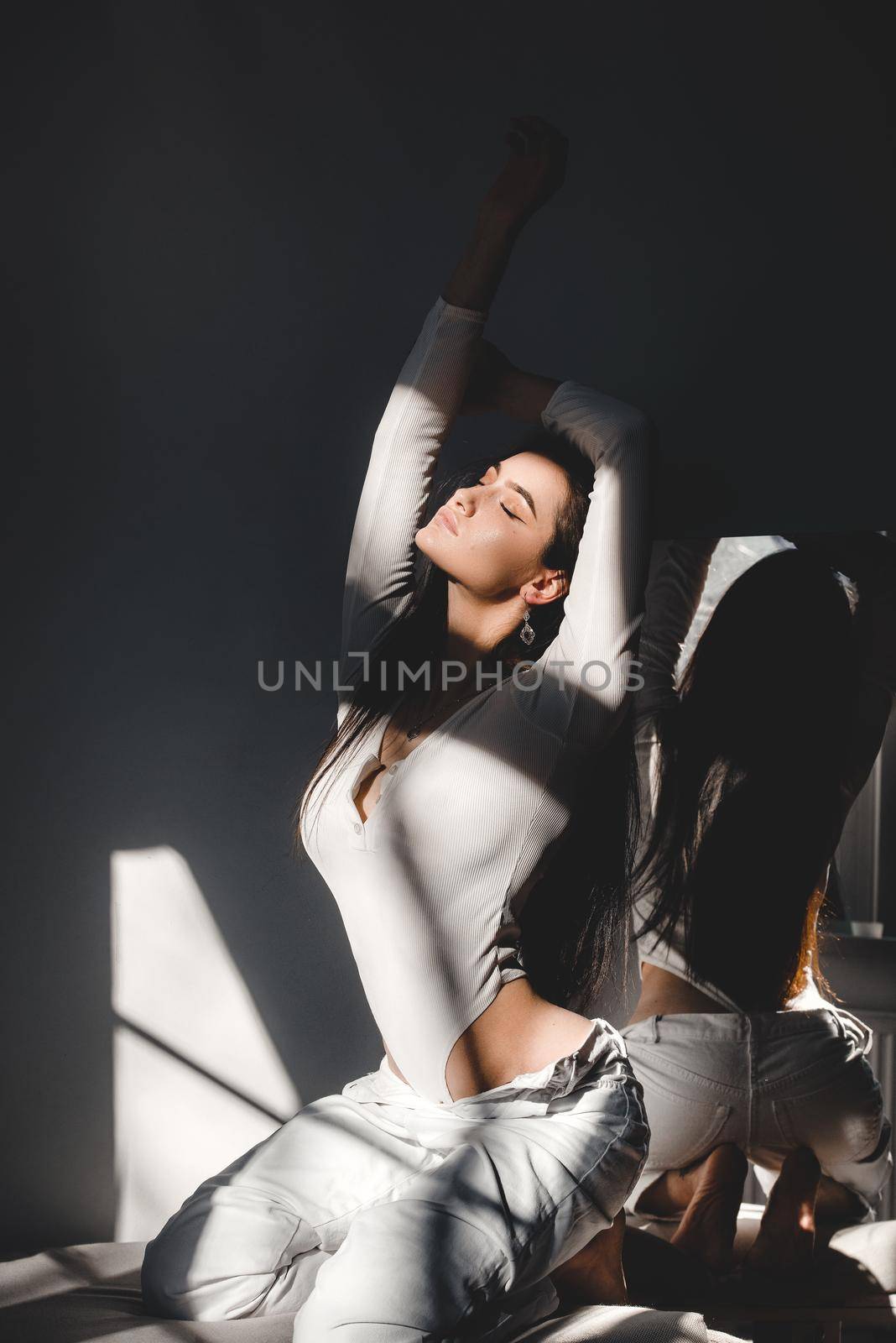 portrait of beautiful gentle woman in a white bodysuit posing in the sunshine. Black long hair. sensuality and tenderness.