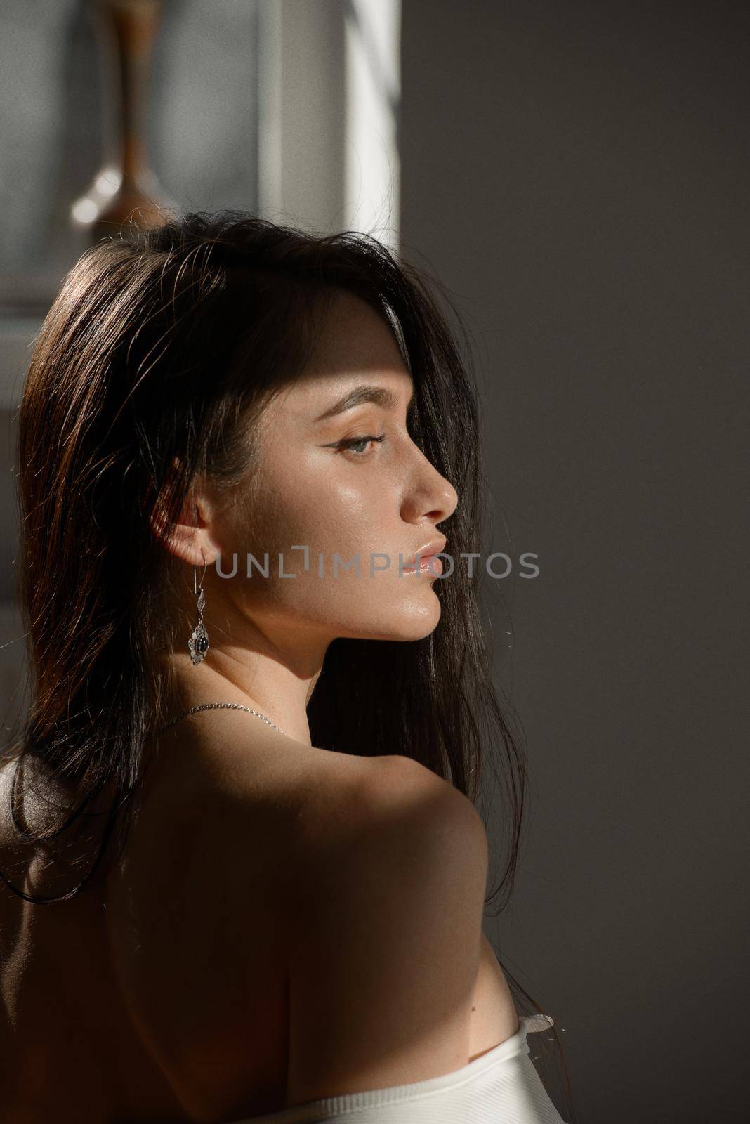 portrait of beautiful gentle woman in a white bodysuit posing in the sunshine. Black long hair. sensuality and tenderness.