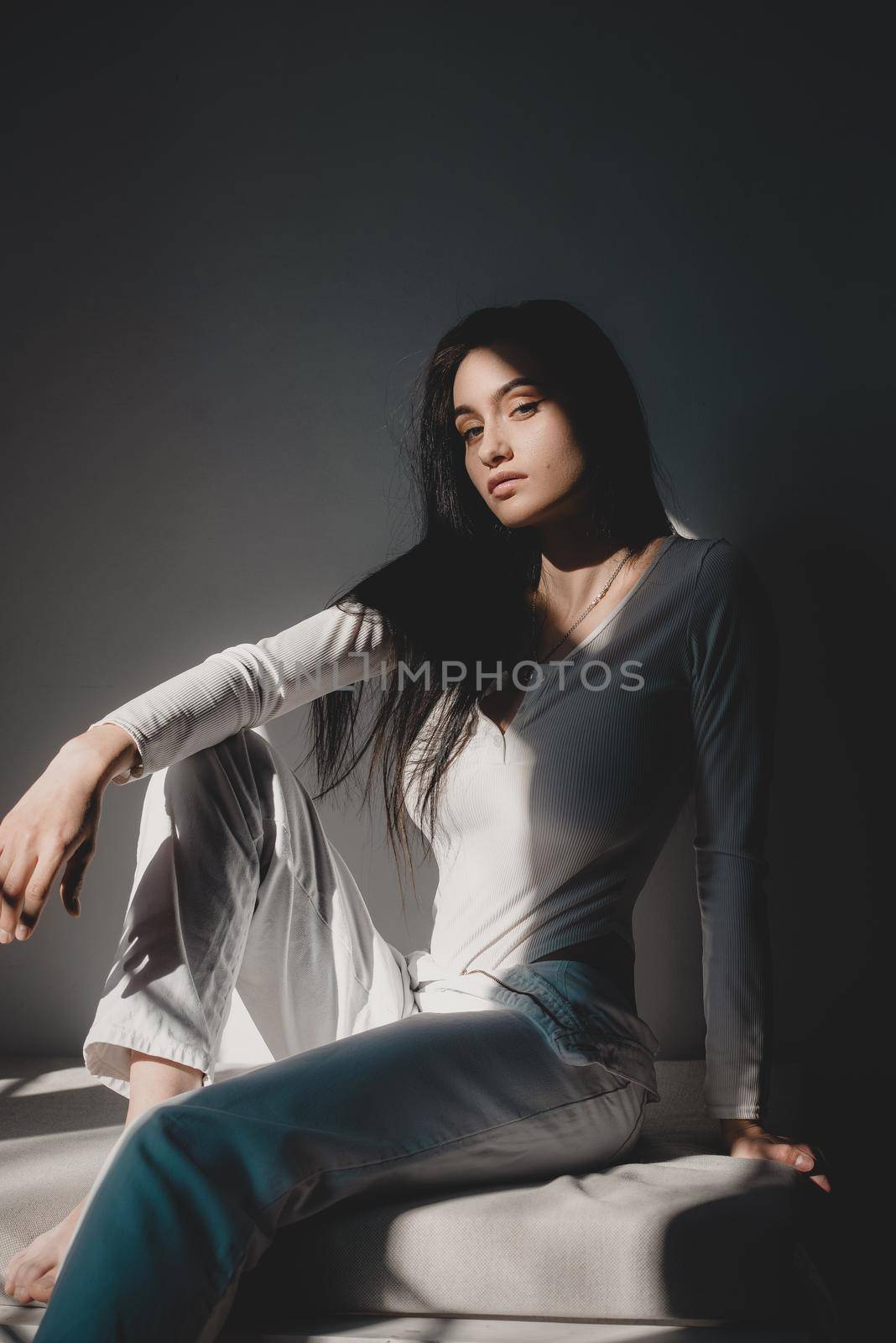 portrait of beautiful gentle woman in a white bodysuit posing in the sunshine. Black long hair. sensuality and tenderness.