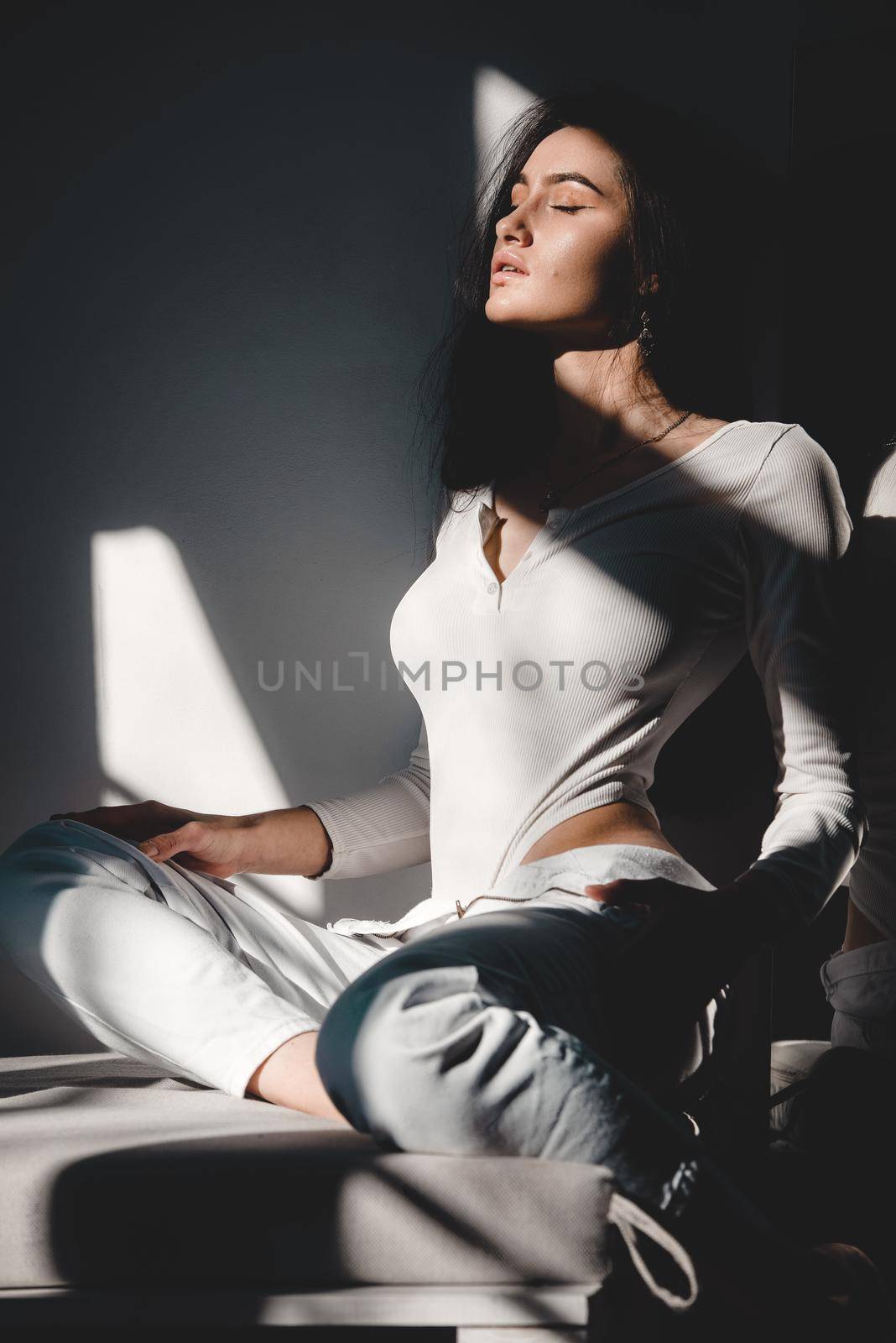 portrait of beautiful gentle woman in a white bodysuit posing in the sunshine. Black long hair. sensuality and tenderness.